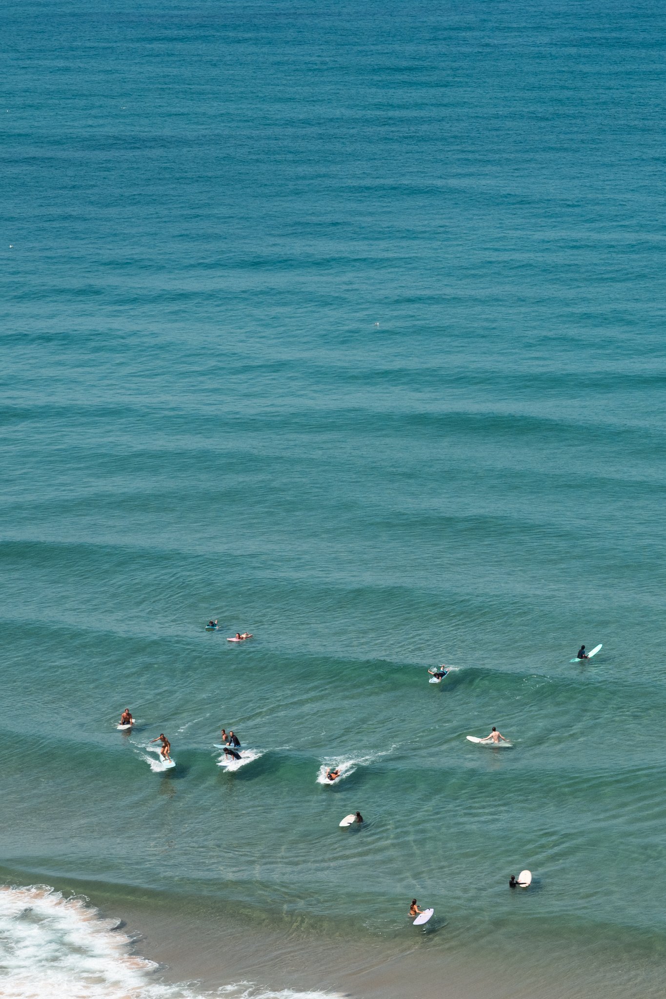 People surfing and floating on the ocean near a sandy beach with calm waves.
