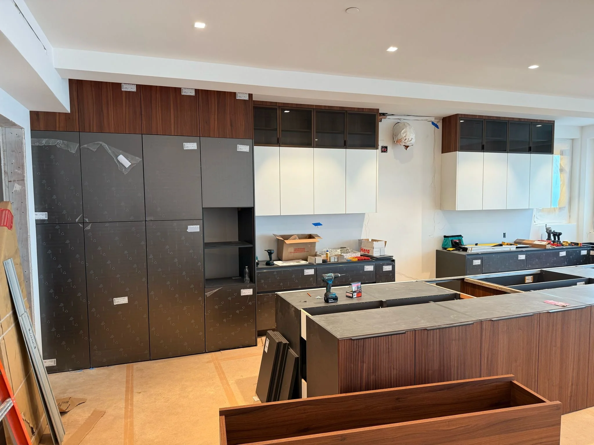 In-progress European kitchen cabinetry installation showing field coordination, cabinet placement, island assembly, and finish protection by UCON Contemporary Interiors.