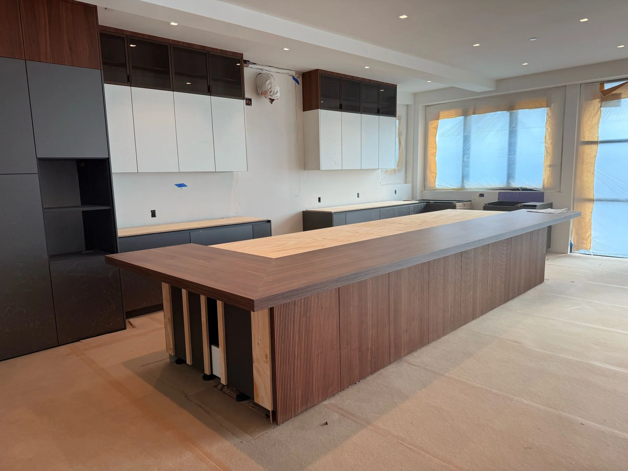 In-progress European kitchen cabinetry installation showing island panel alignment, cabinet layout, appliance openings, and field verification by UCON Contemporary Interiors.