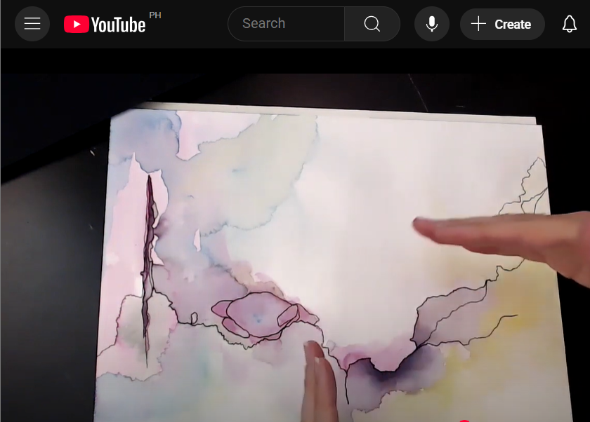 A snapshot of a Youtube video from Mindful Creative Muse, teaching art journal ideas. A hand is demonstrating in front of the camera about an artwork on a sketchbook.