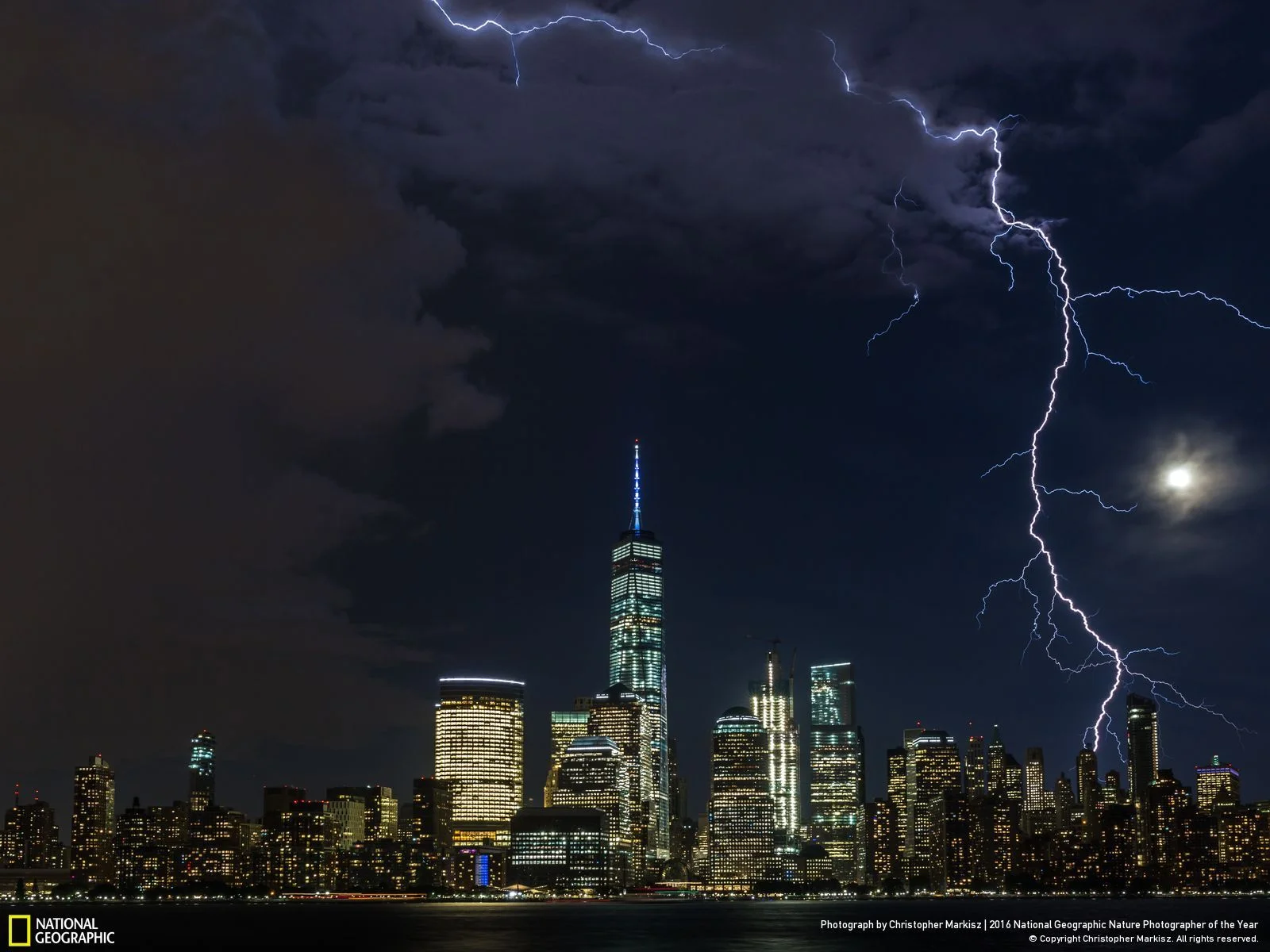 Moonlighting by Christopher Markisz: Lightning strikes lower Manhattan as a summer storm approaches a moonlit New York City skyline. Location: United States
