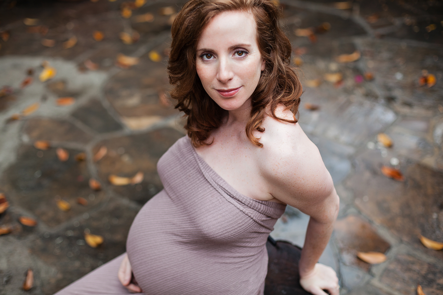 expecting mother holding her belly with a leaf-covered ground
