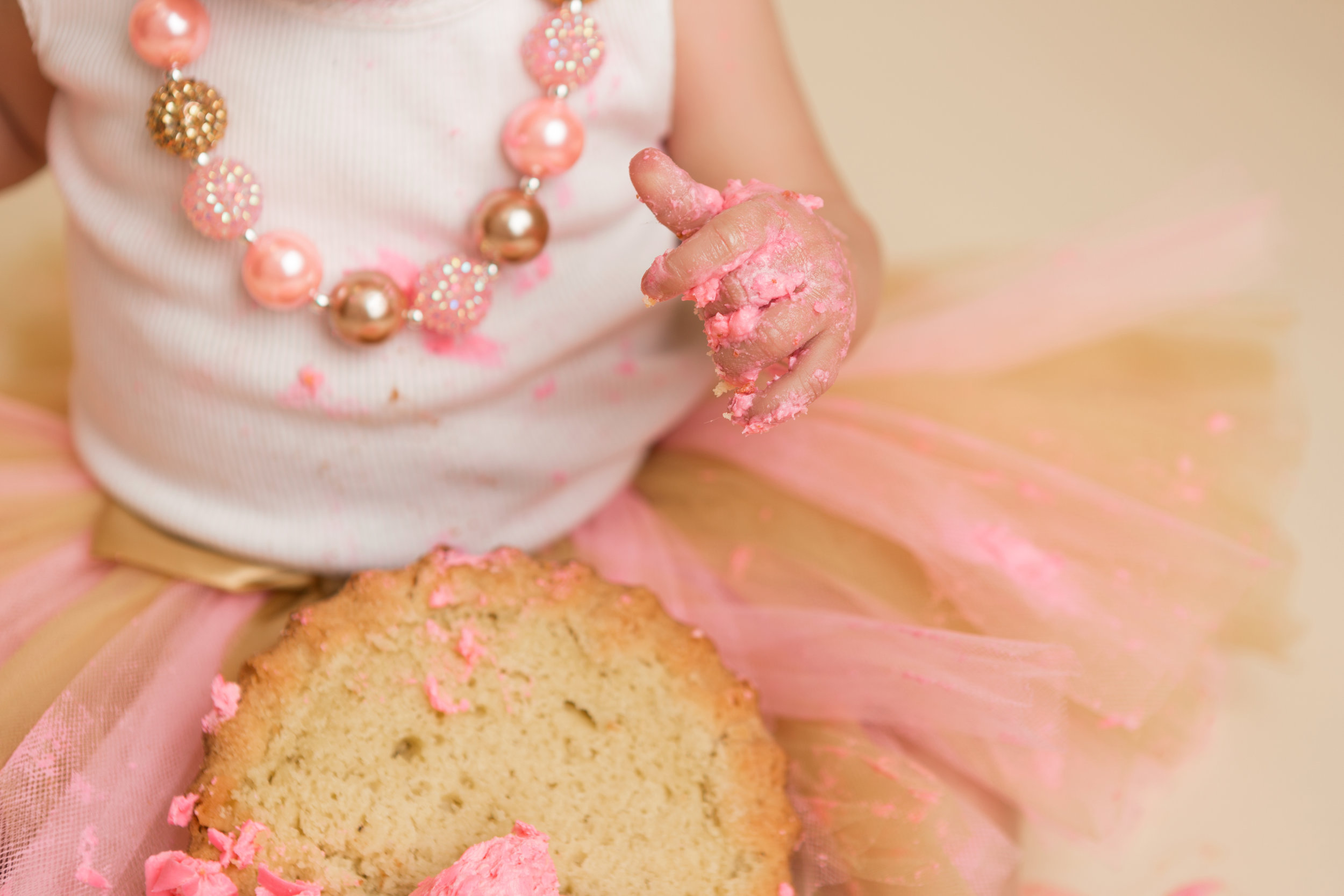 messy aftermath of a birthday cake smash- a baby's hand with pink frosting