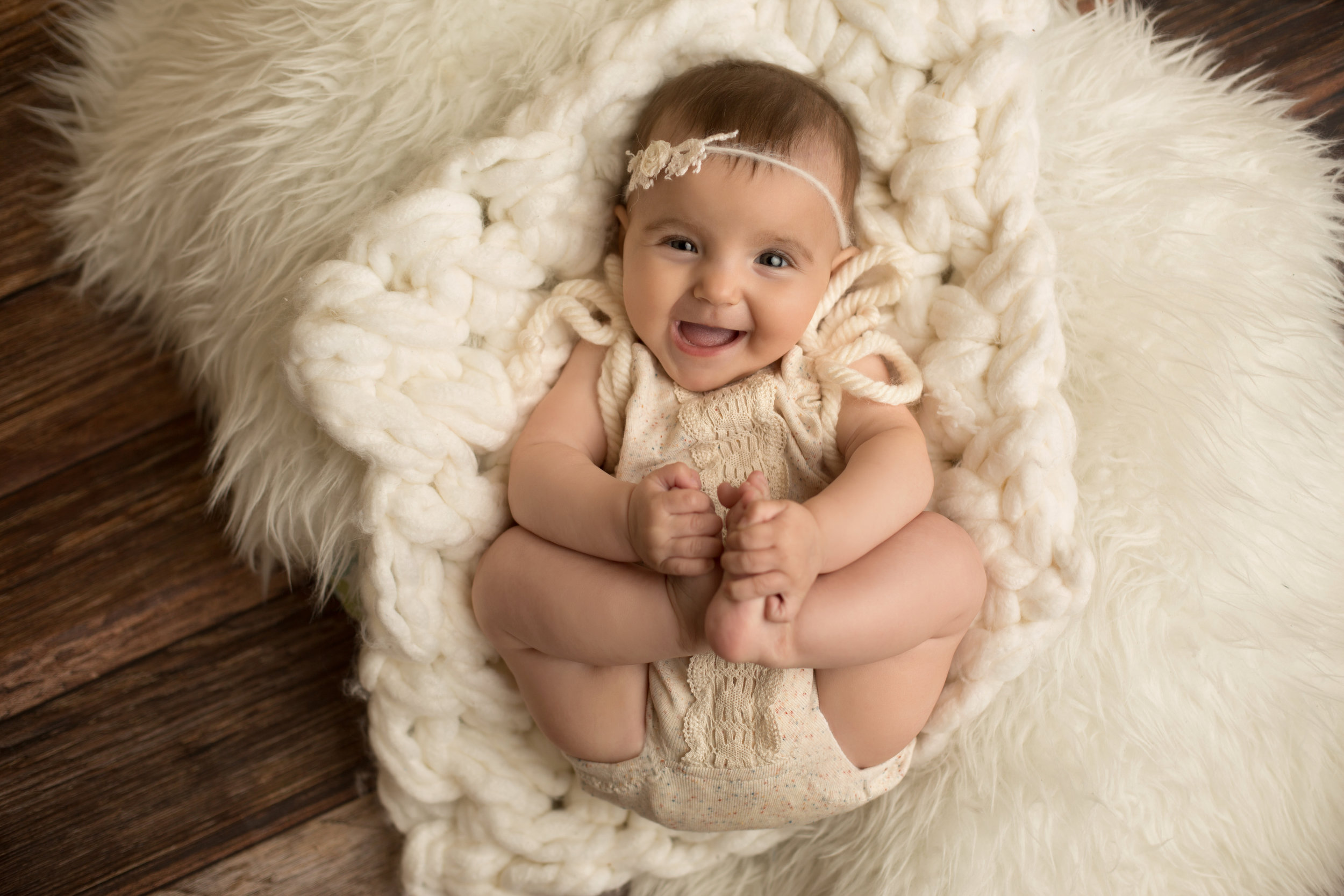 1 year old girl holding her feet while laying on a cream fur rug