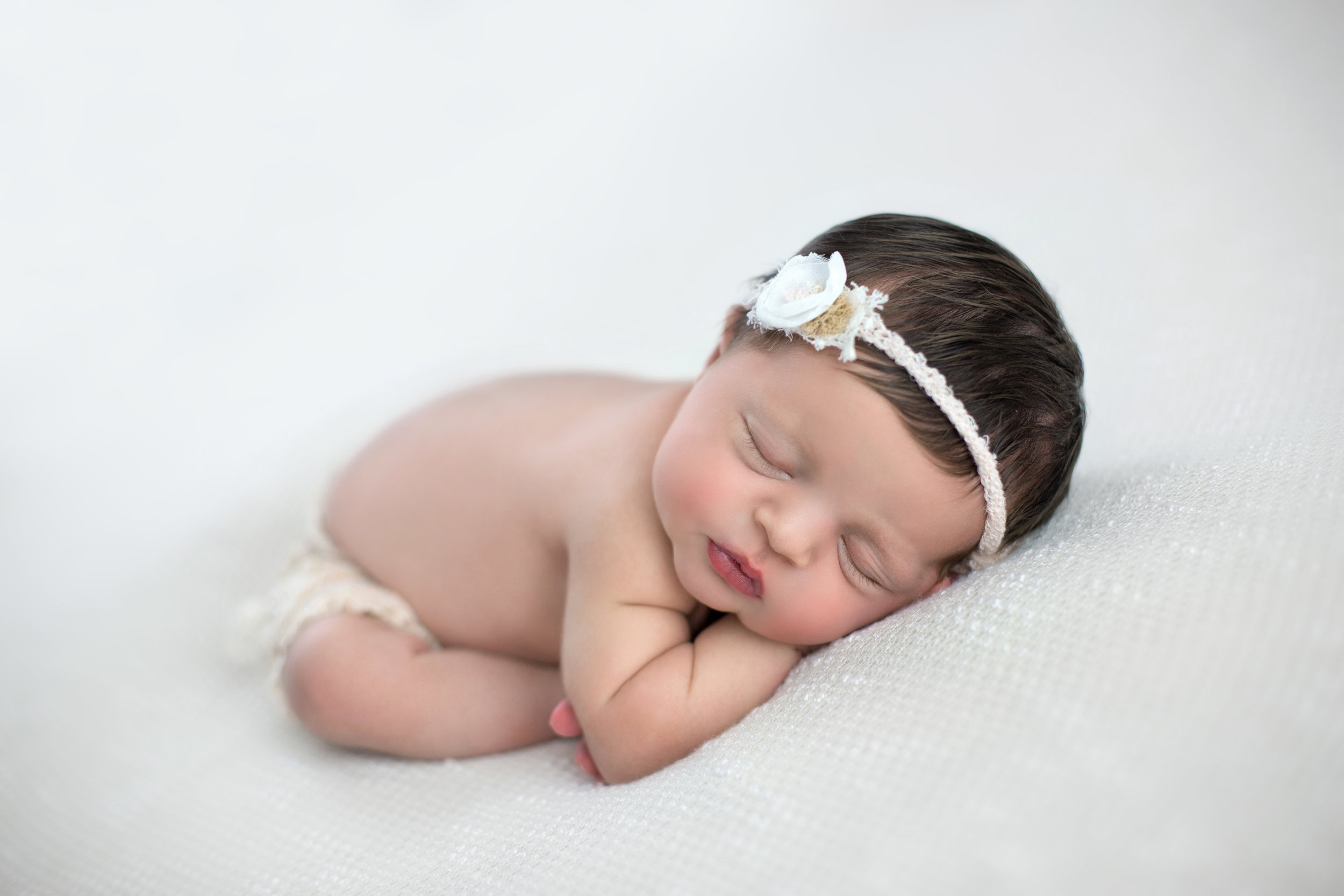 newborn with a white headband sleeping on her stomach