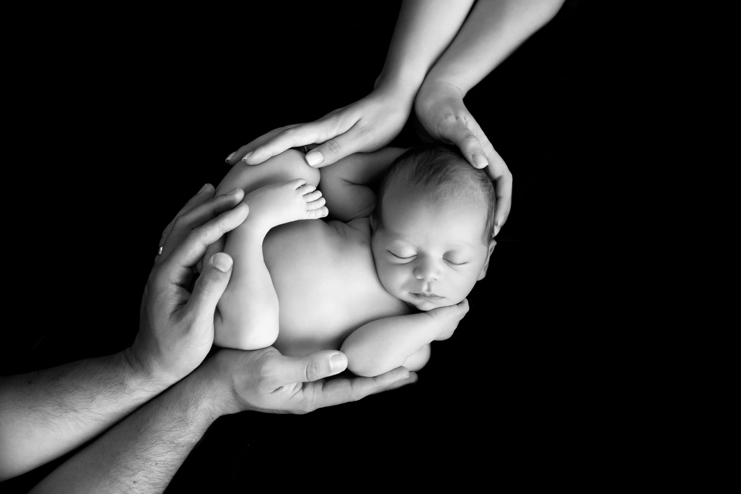 a baby surrounded by his mom and dad's hands on black fabric 