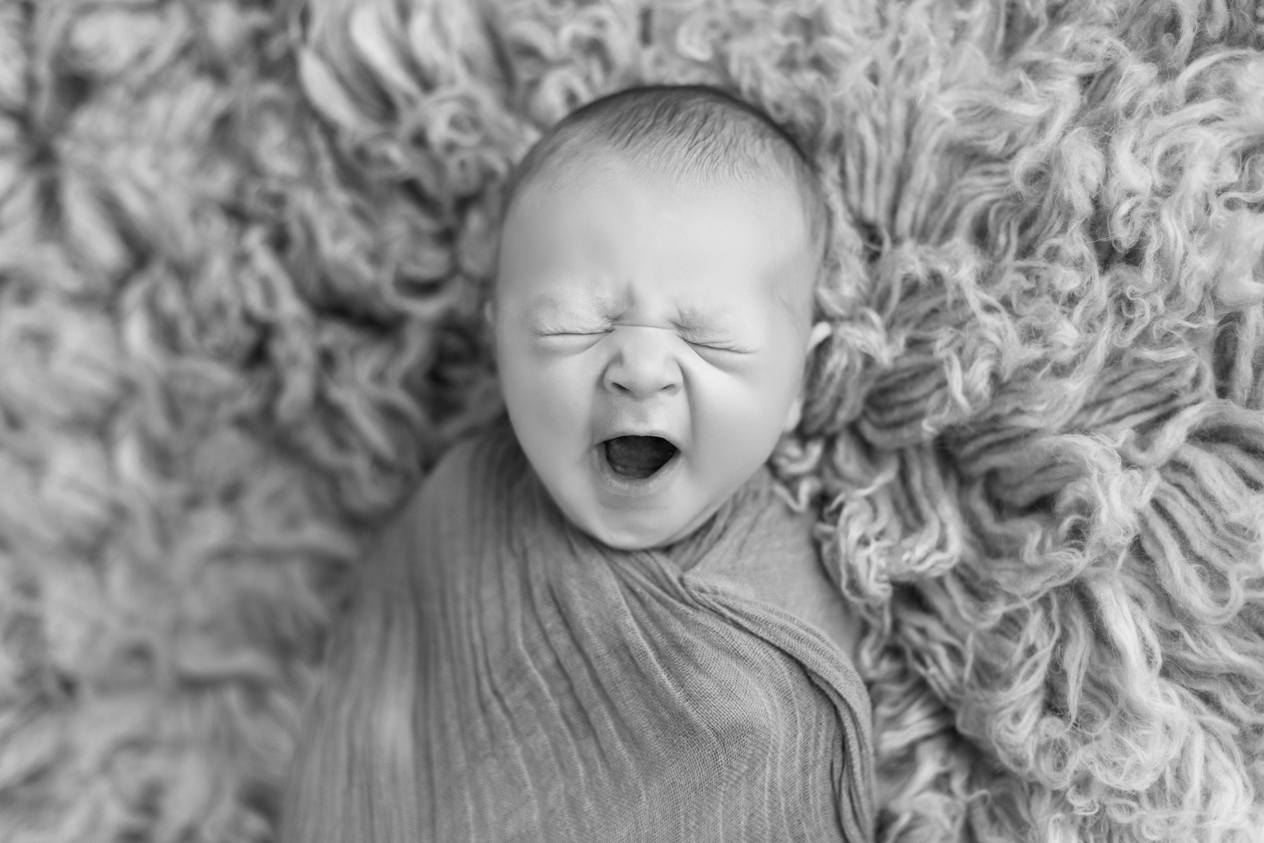  baby boy yawning as he lays on a fuzzy rug in black and white
