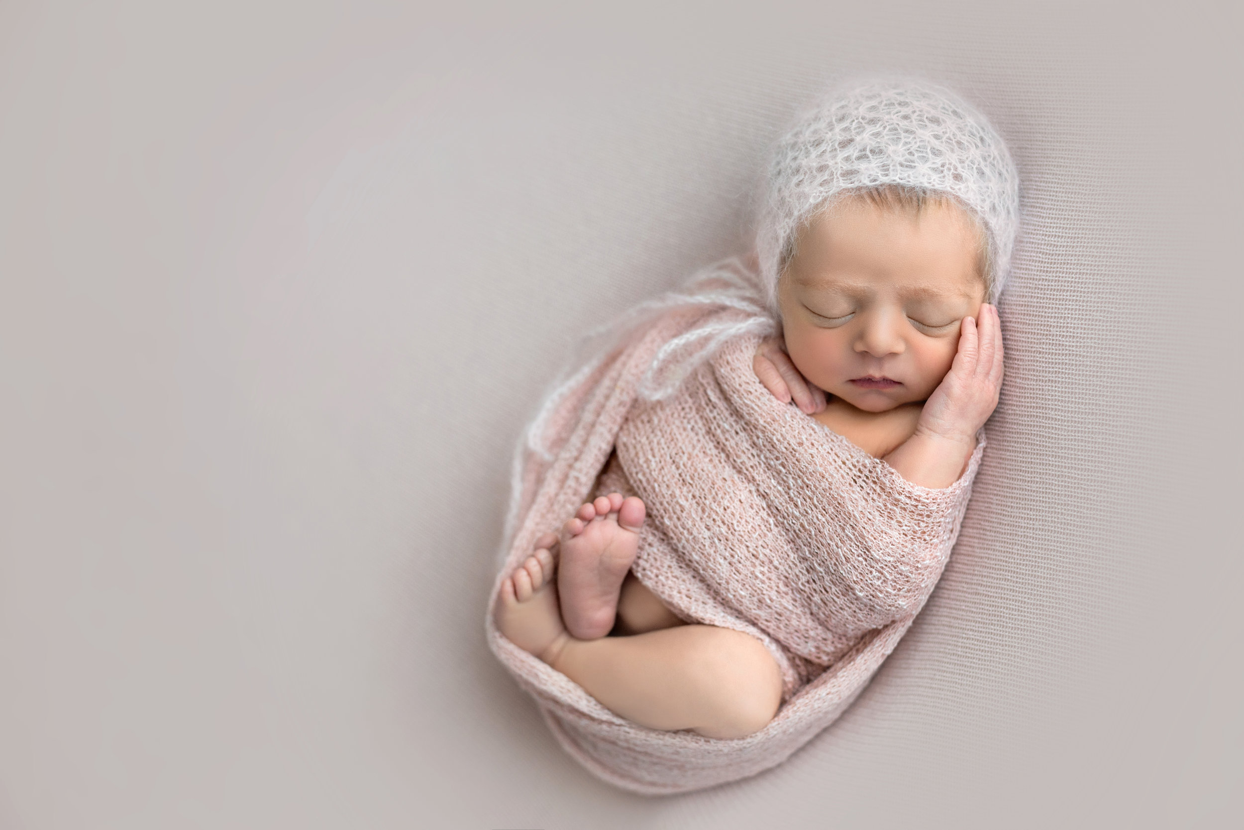 baby girl wrapped in light pink with a white bonnet asleep