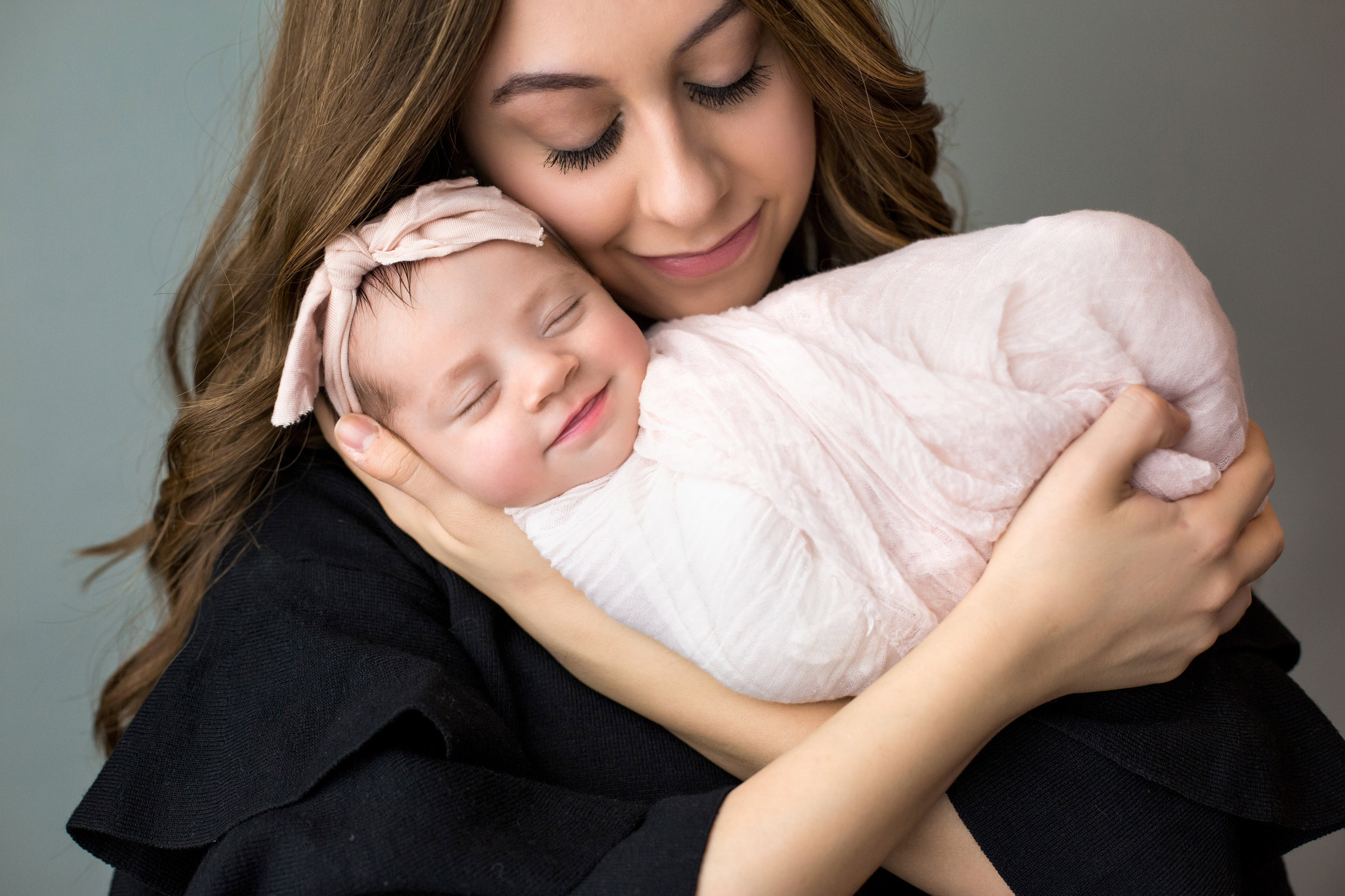 mom and newborn wrapped in pink smiling as they snuggle together