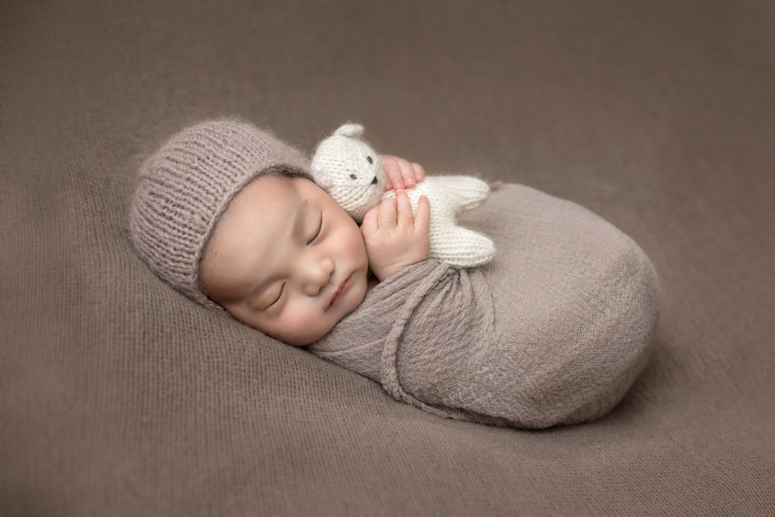 adorable baby in brown hugging a small white teddy bear