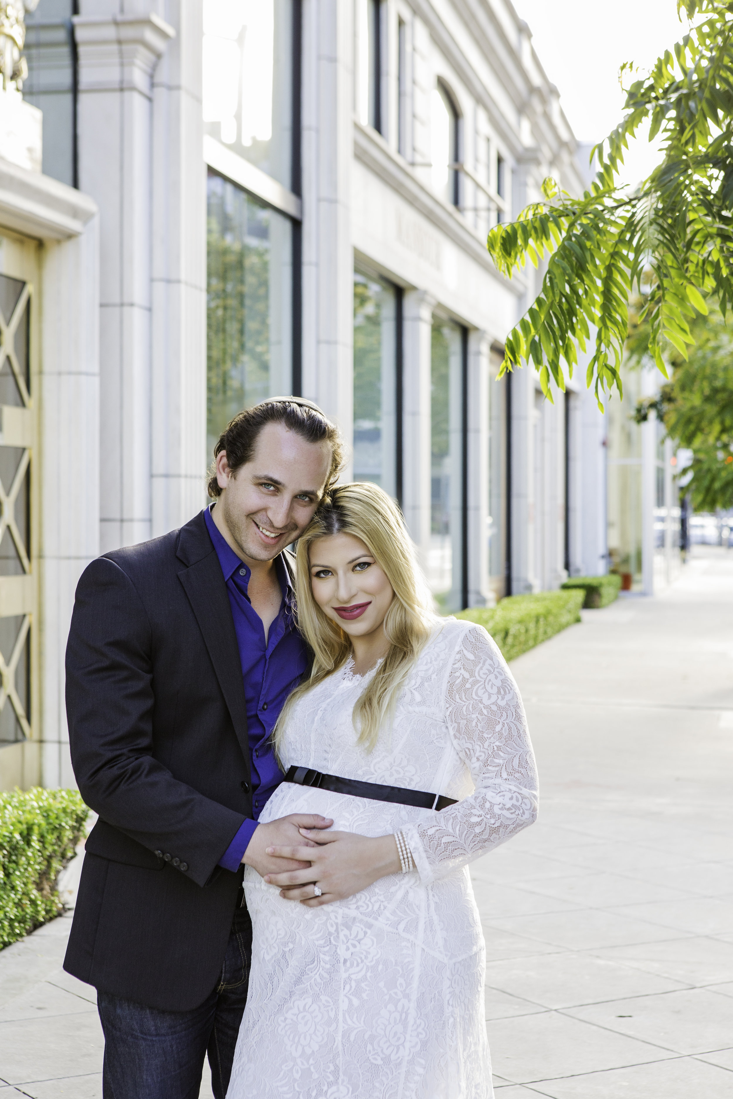 excited expecting couple in front of a white building