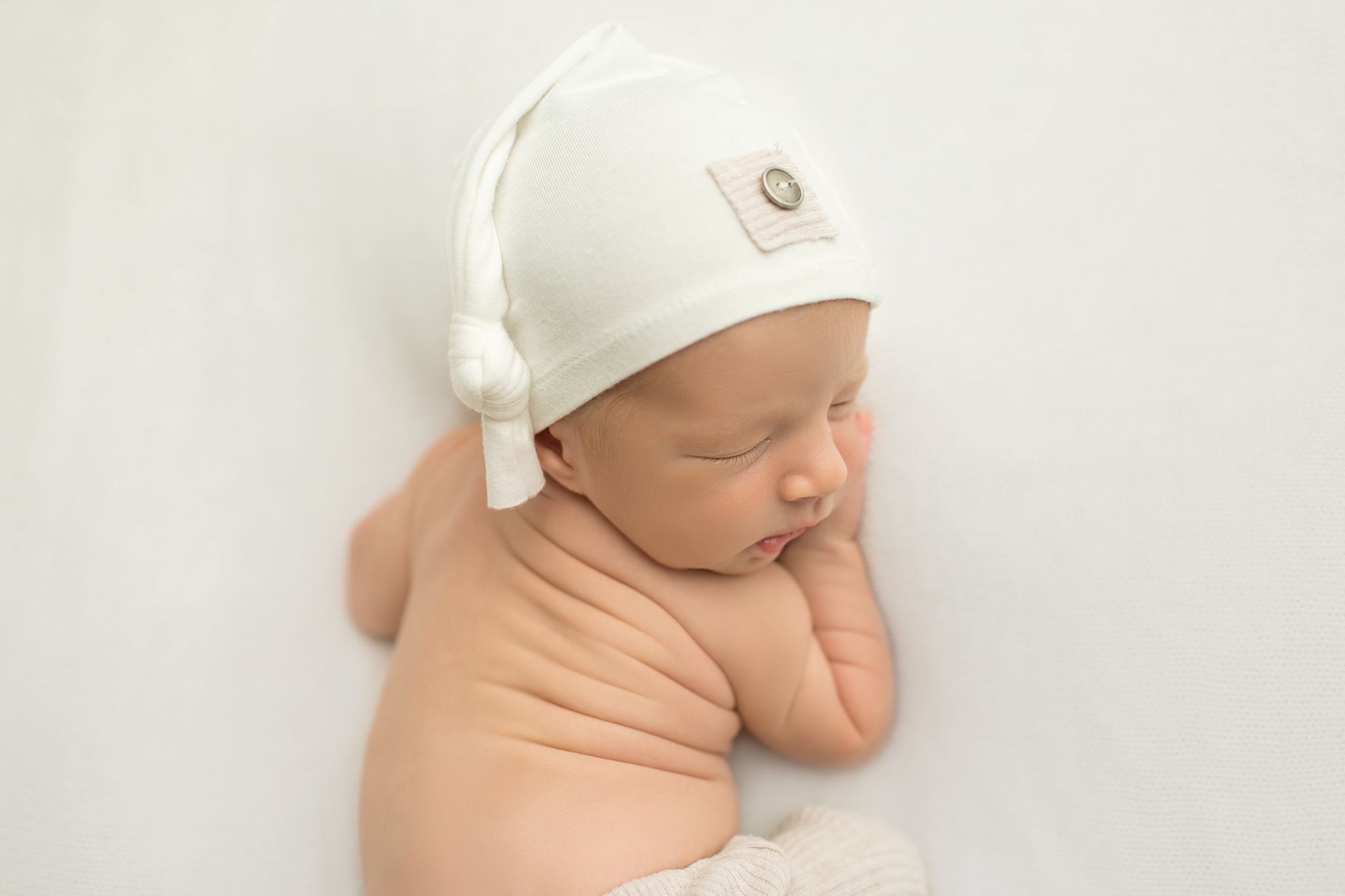 newborn boy with a white sleepy cap on