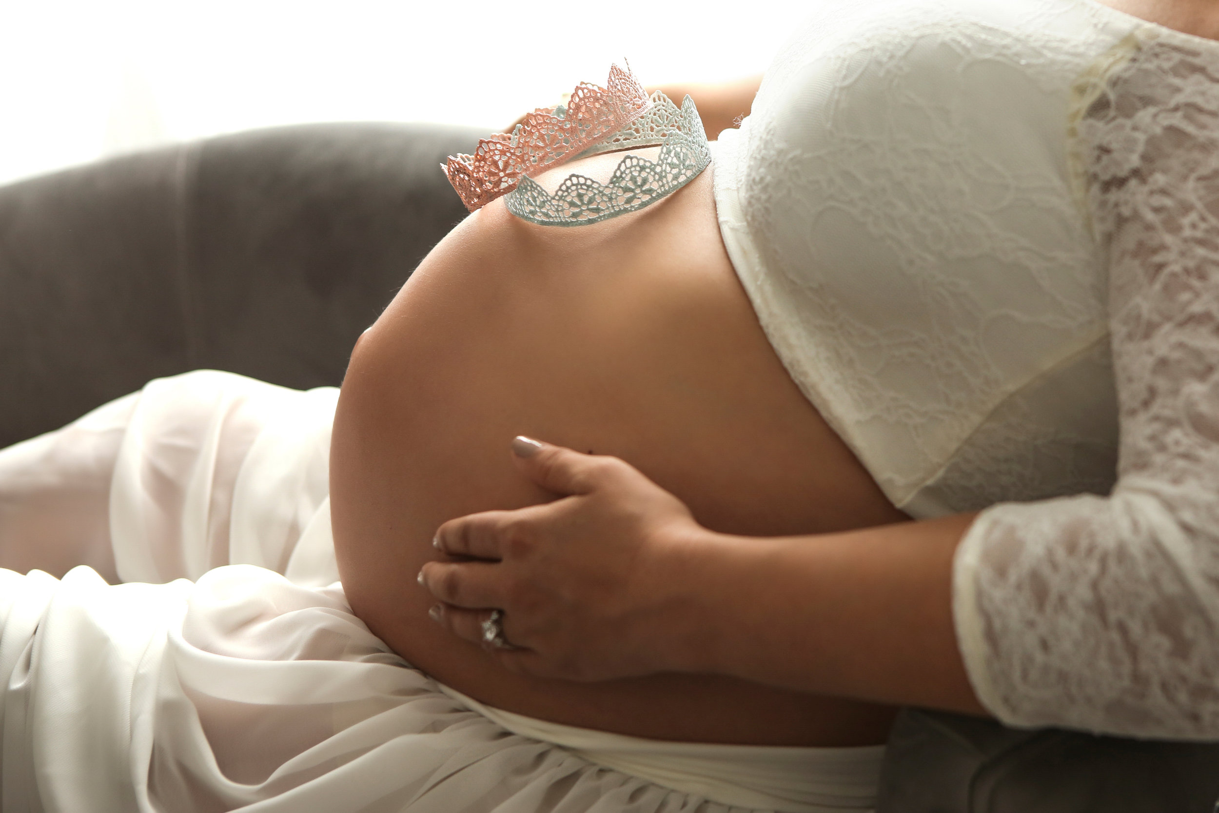 pregnant mom holds her belly, where two crowns are placed