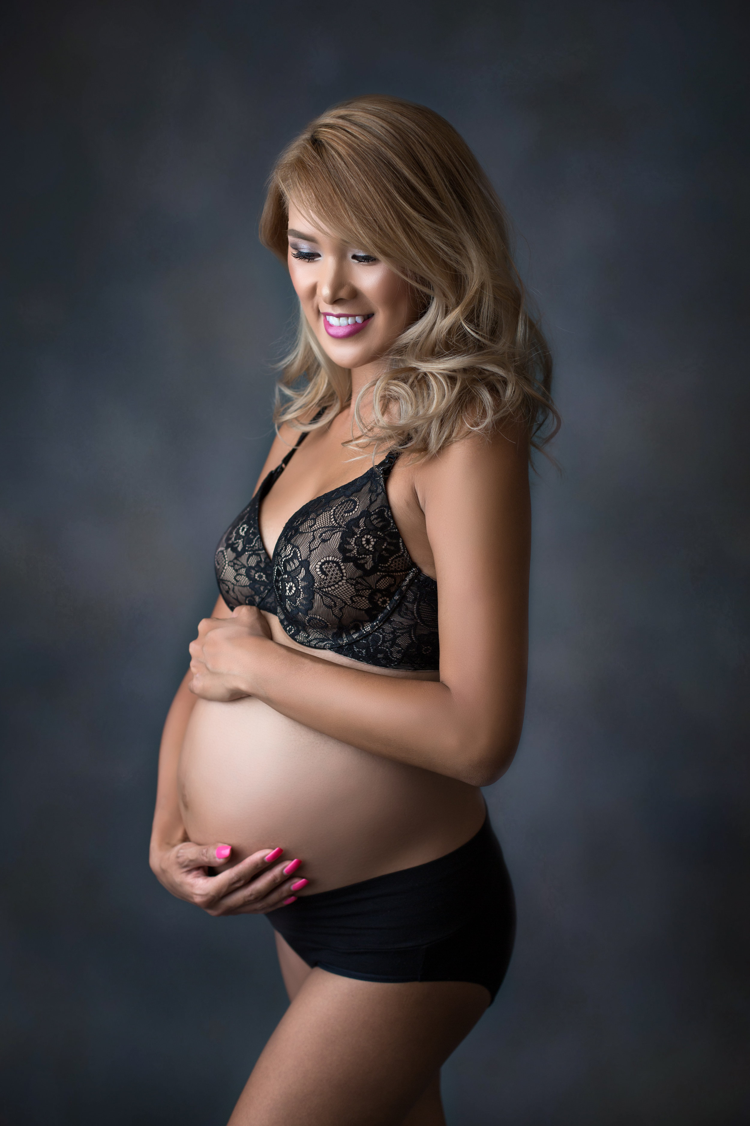 pregnant woman with pink nails smiles and holds her bump