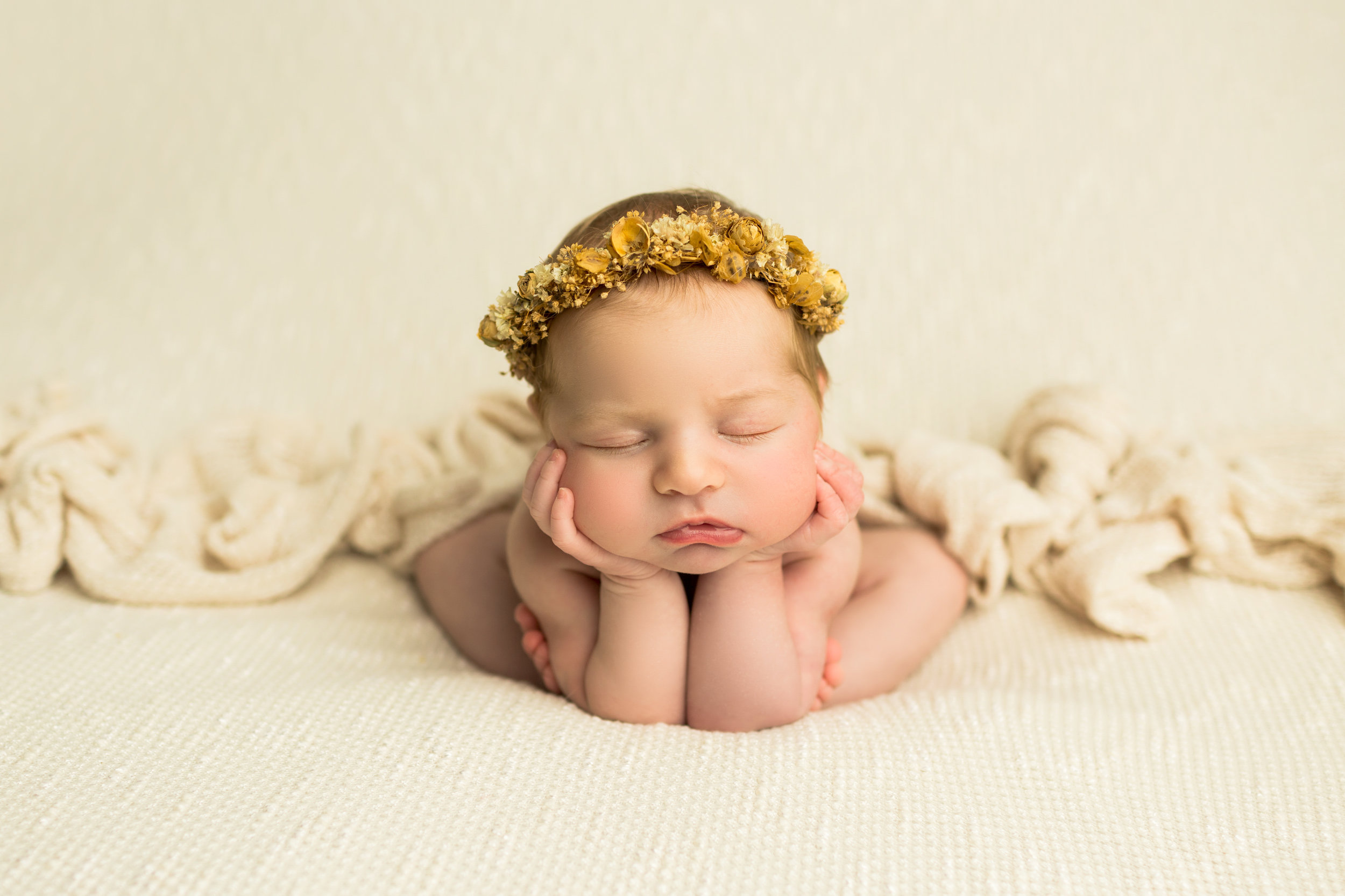 newborn with a yellow floral headband supporting her head on her hands