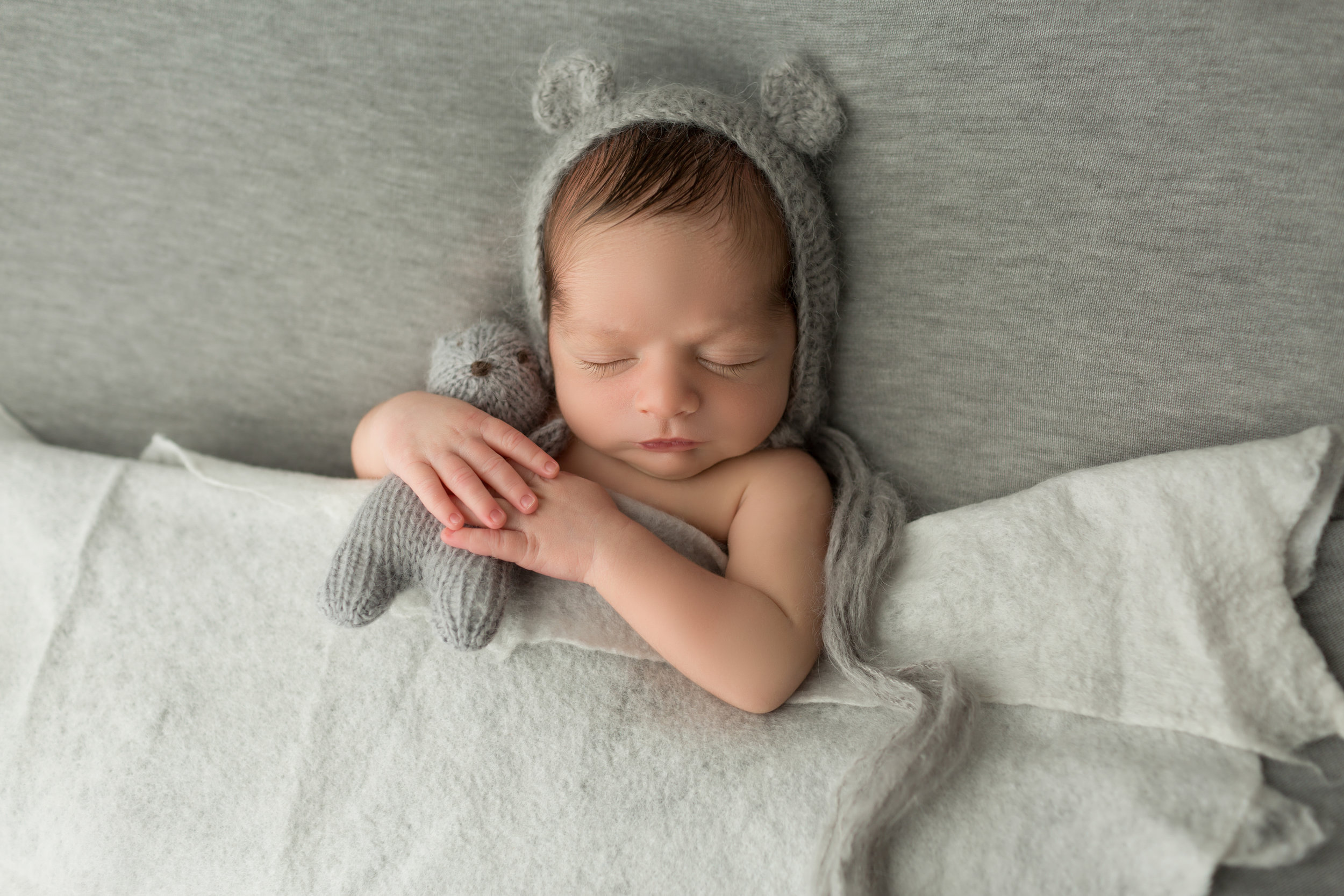 newborn boy in a grey bear hat hugging a toy bear