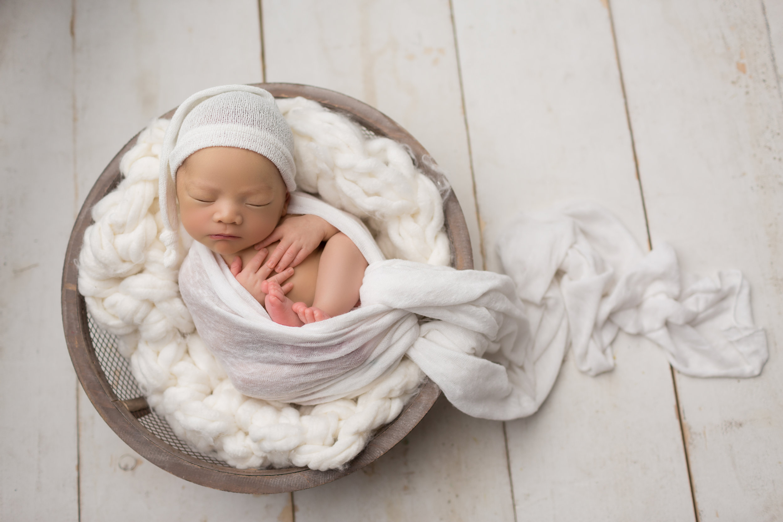 baby boy in bowl snuggled on a white blanket