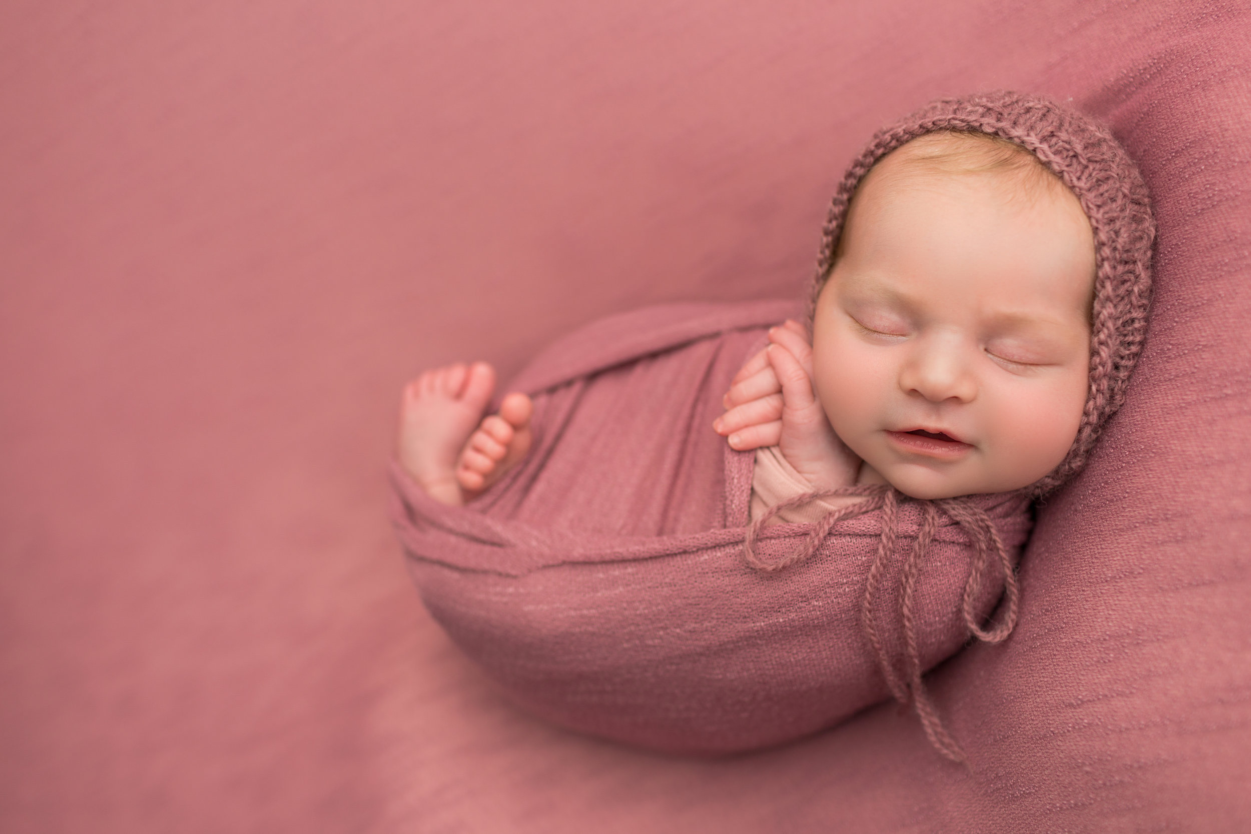 baby girl smiling in her sleep, all wrapped in dark pink