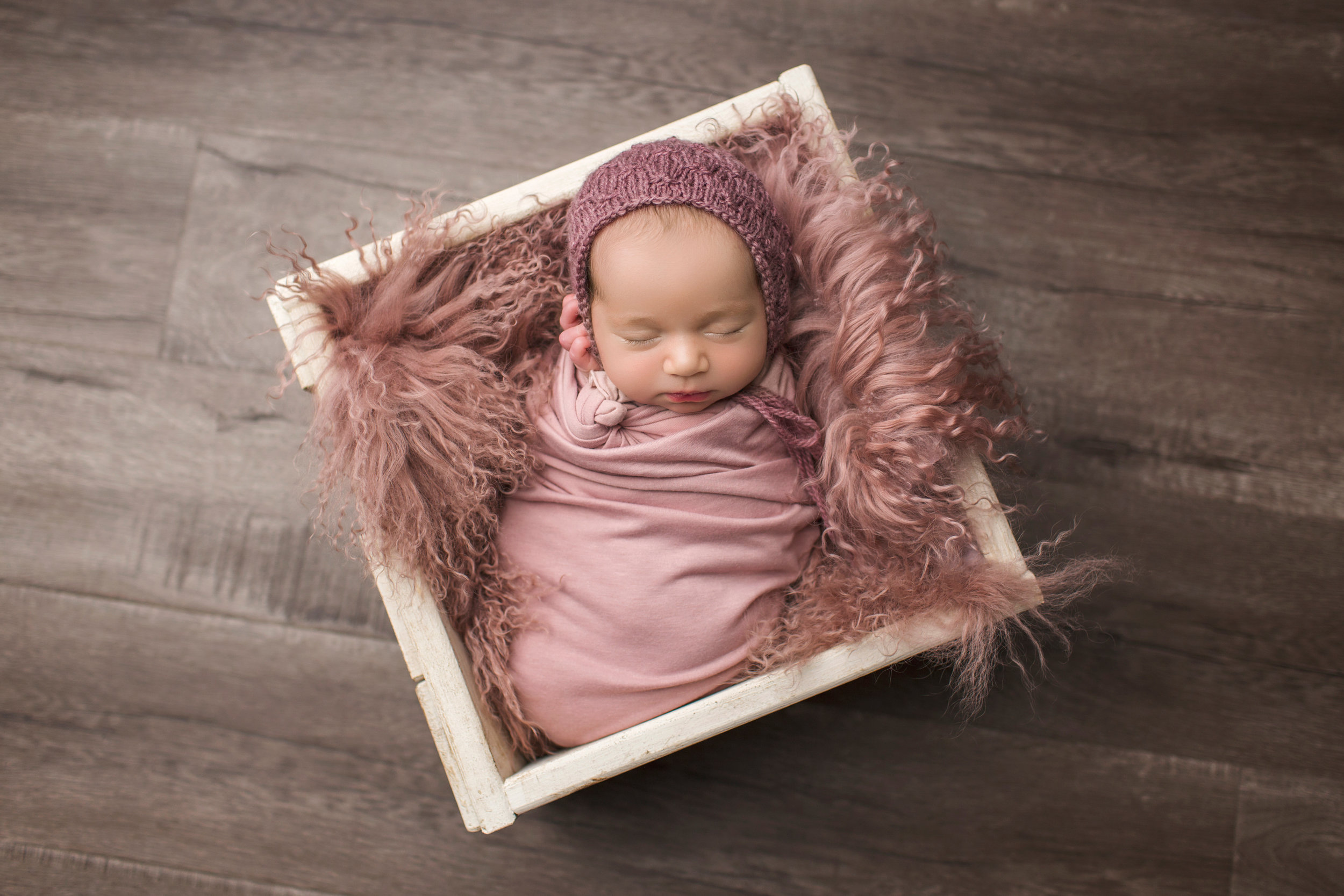 baby girl in box surrounded by dark pink fur rug 