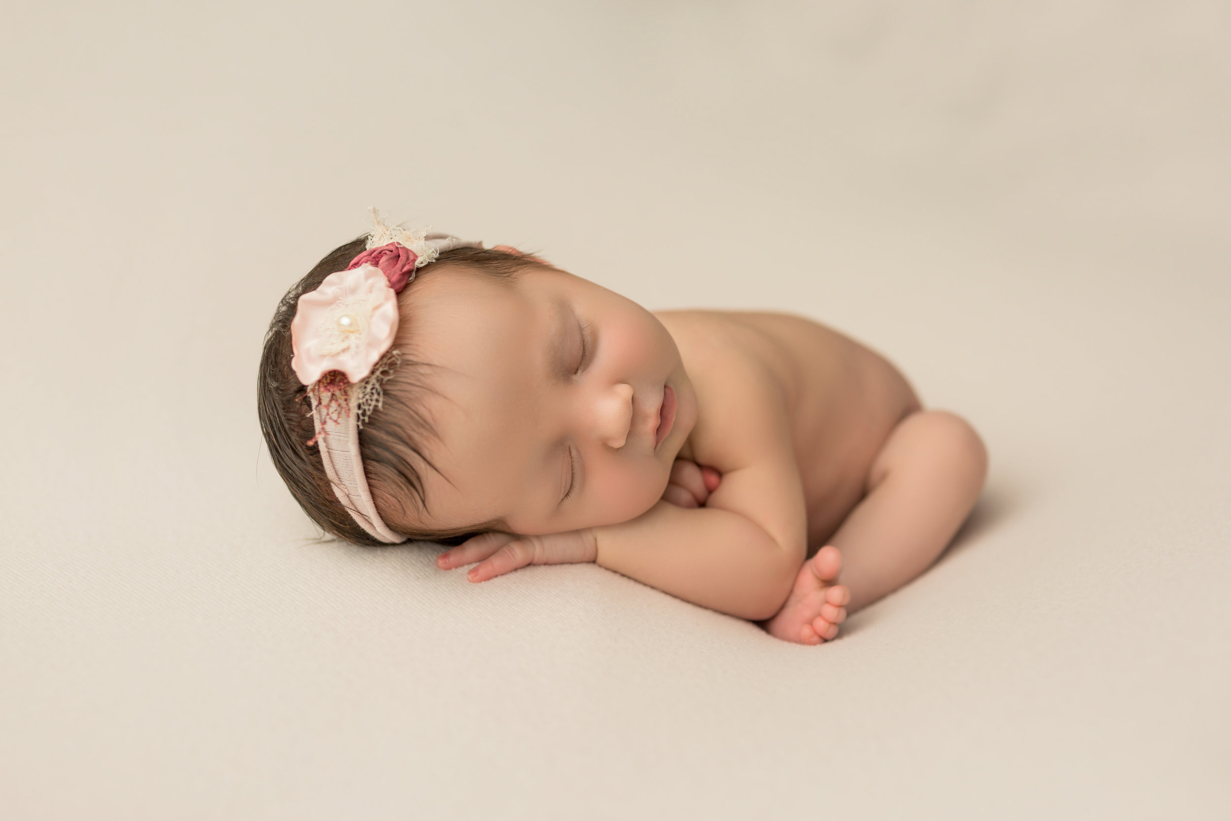 baby girl lying on a cream background with a pink flower headband