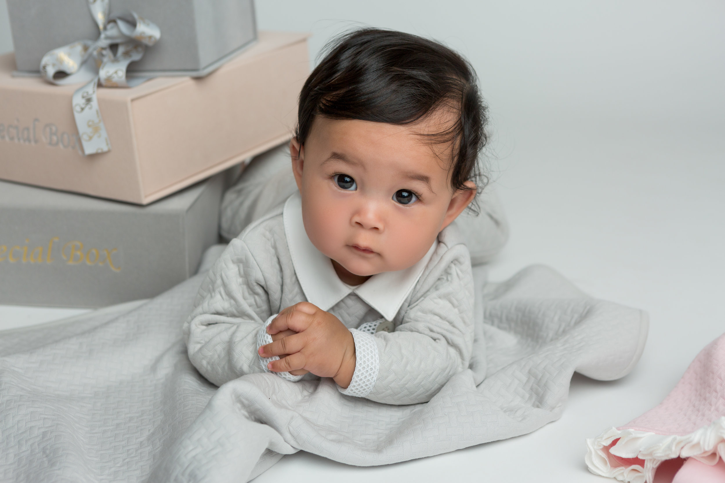 1 year old adorable boy in baby blue, laying next to a stack of gifts