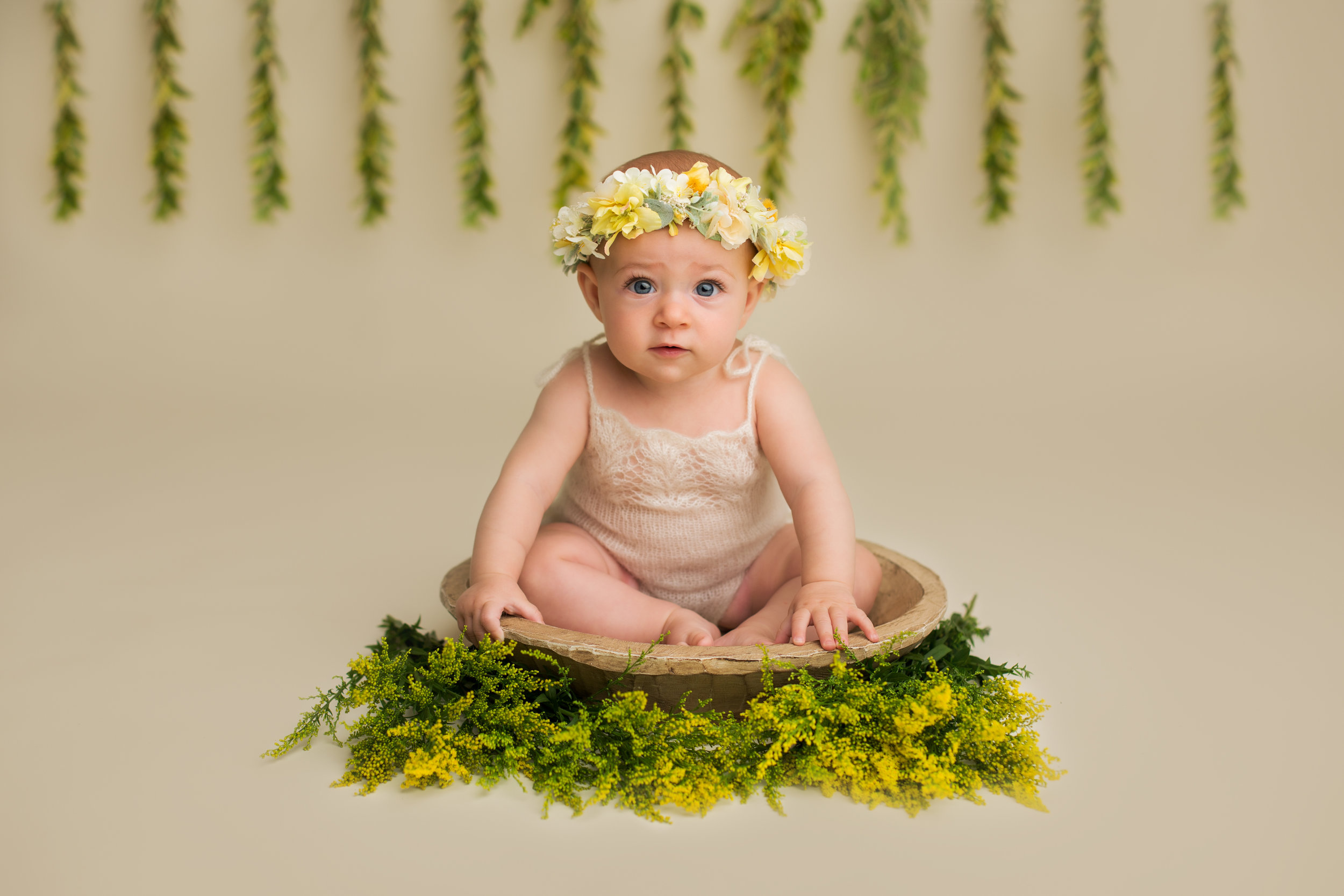 baby girl sitting in a bowl on top of green and yellow flowers