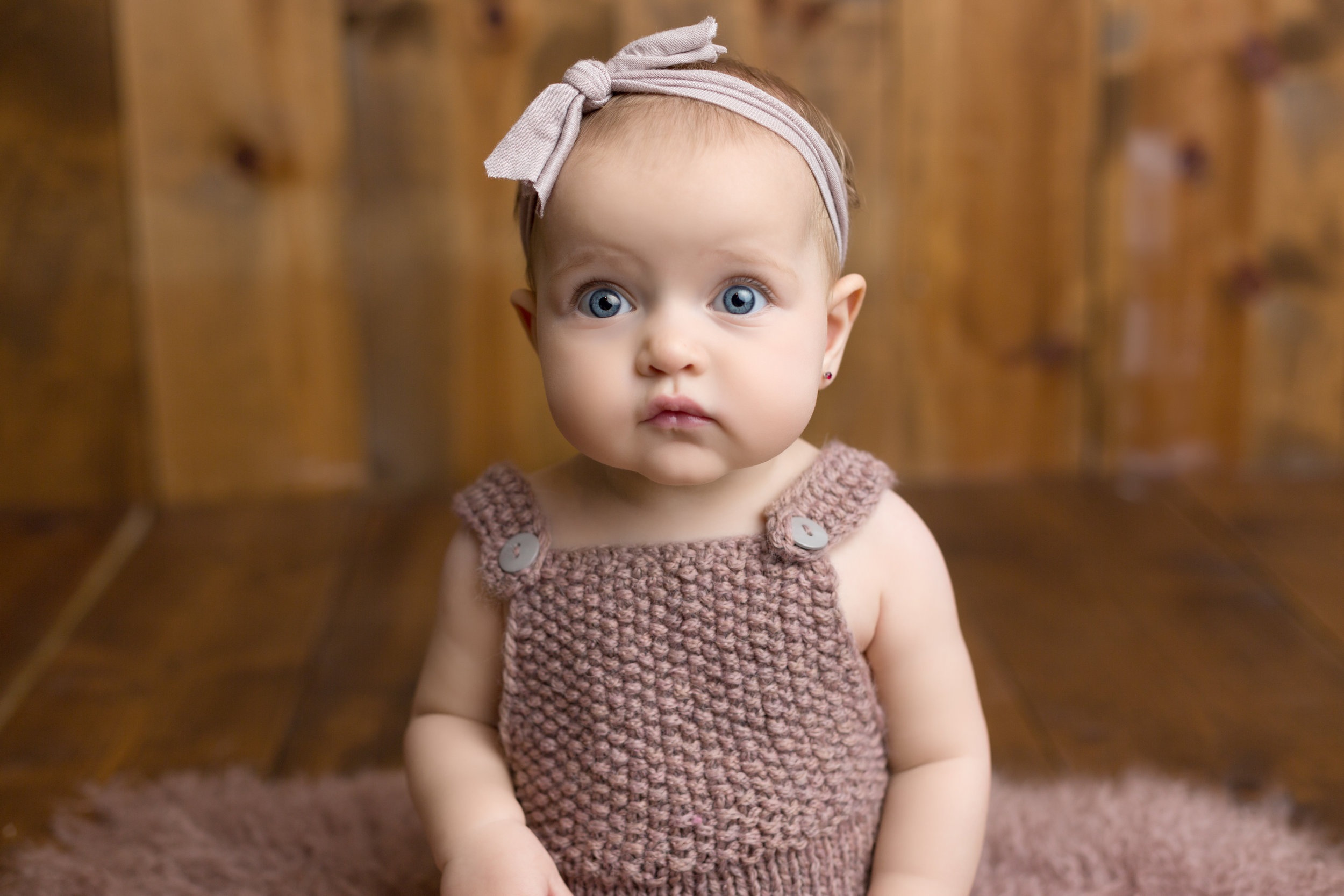 baby girl with blue eyes wearing purple knit overalls stares into the camera