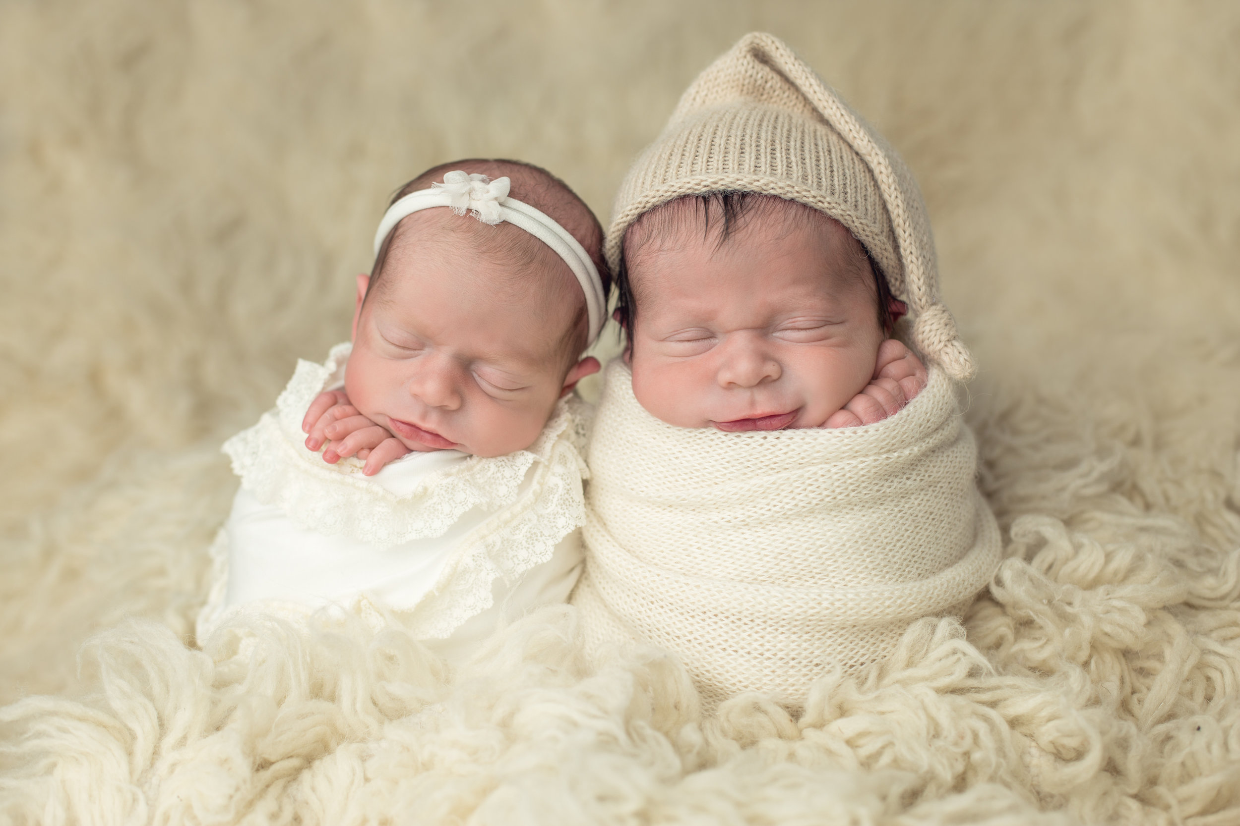 twin newborns with neutral wraps on a cream furry rug