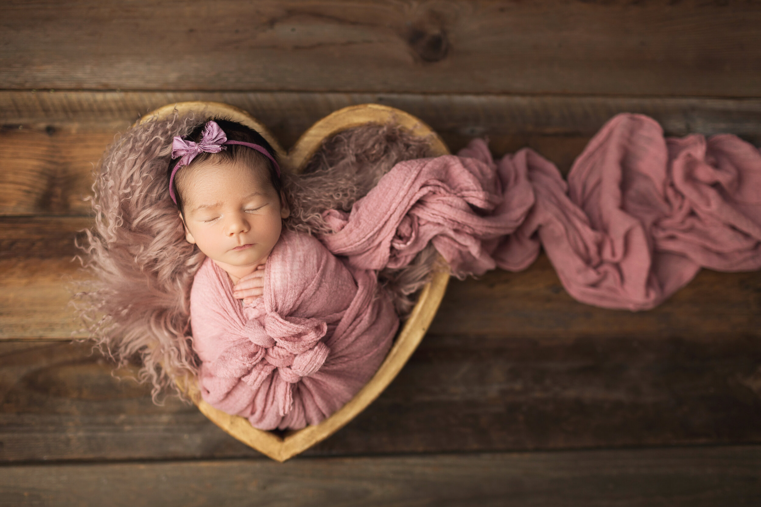 baby girl in a heart bowl on a wood floor with her wrap trailing to the right