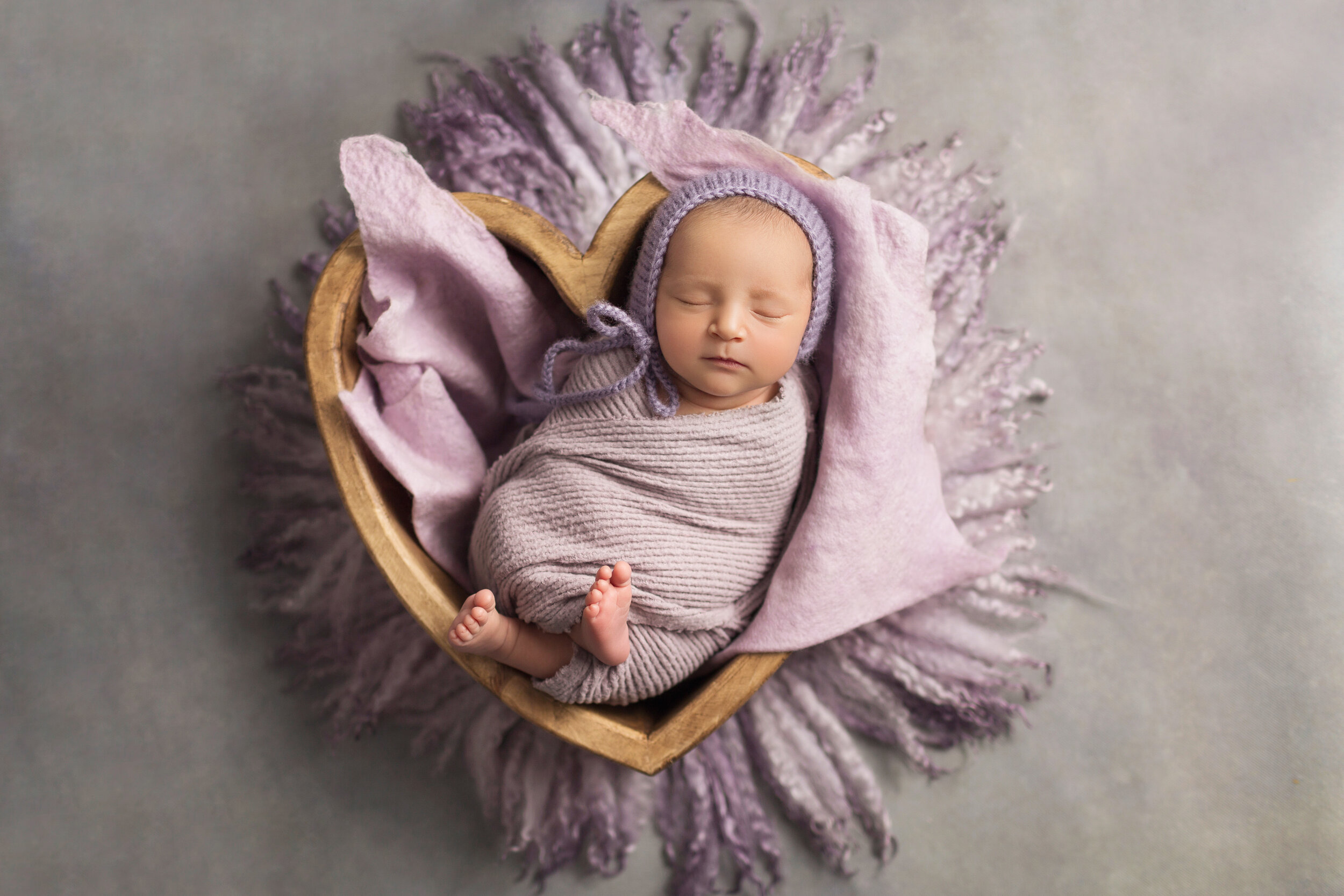 baby sleeping in a heart bowl wrapped in lavender on a purple fur rug