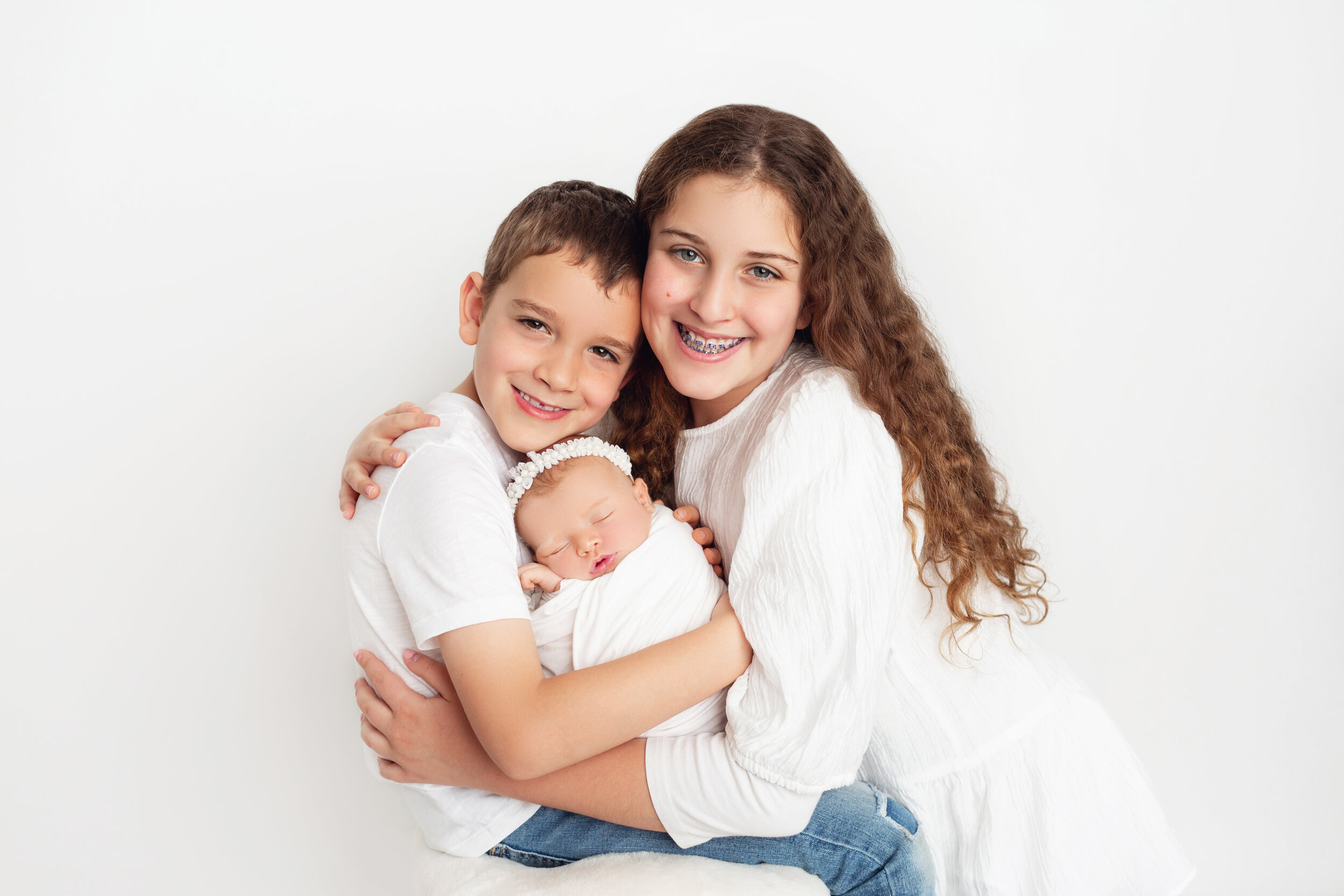 oldest sister hugs her brother, who is holding their newborn sister close