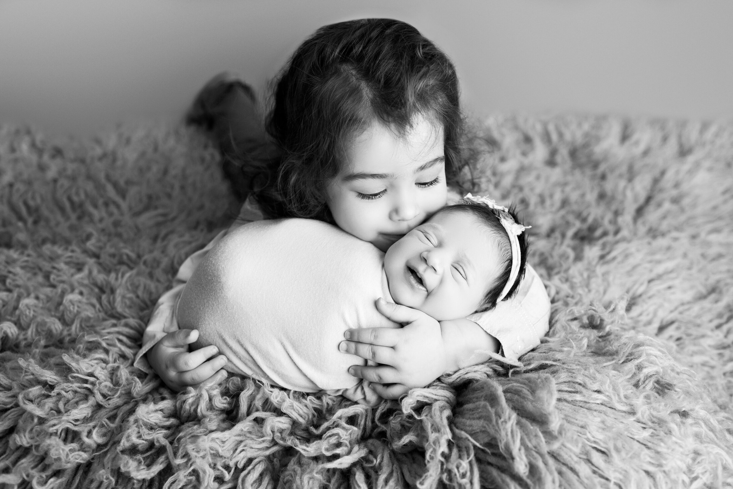 older sibling planting a kiss on his newborn sisters cheek while she smiles