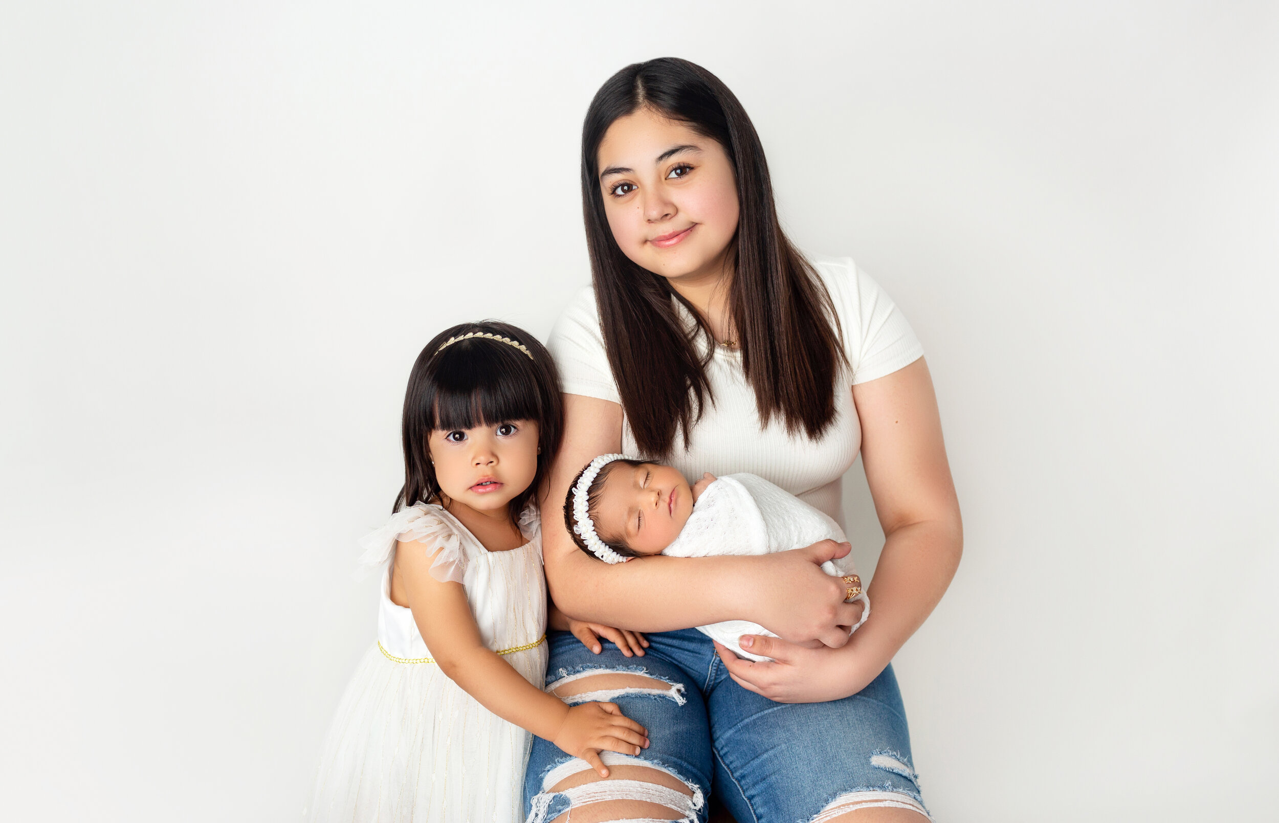 two sisters look at the camera while holding their newborn sister