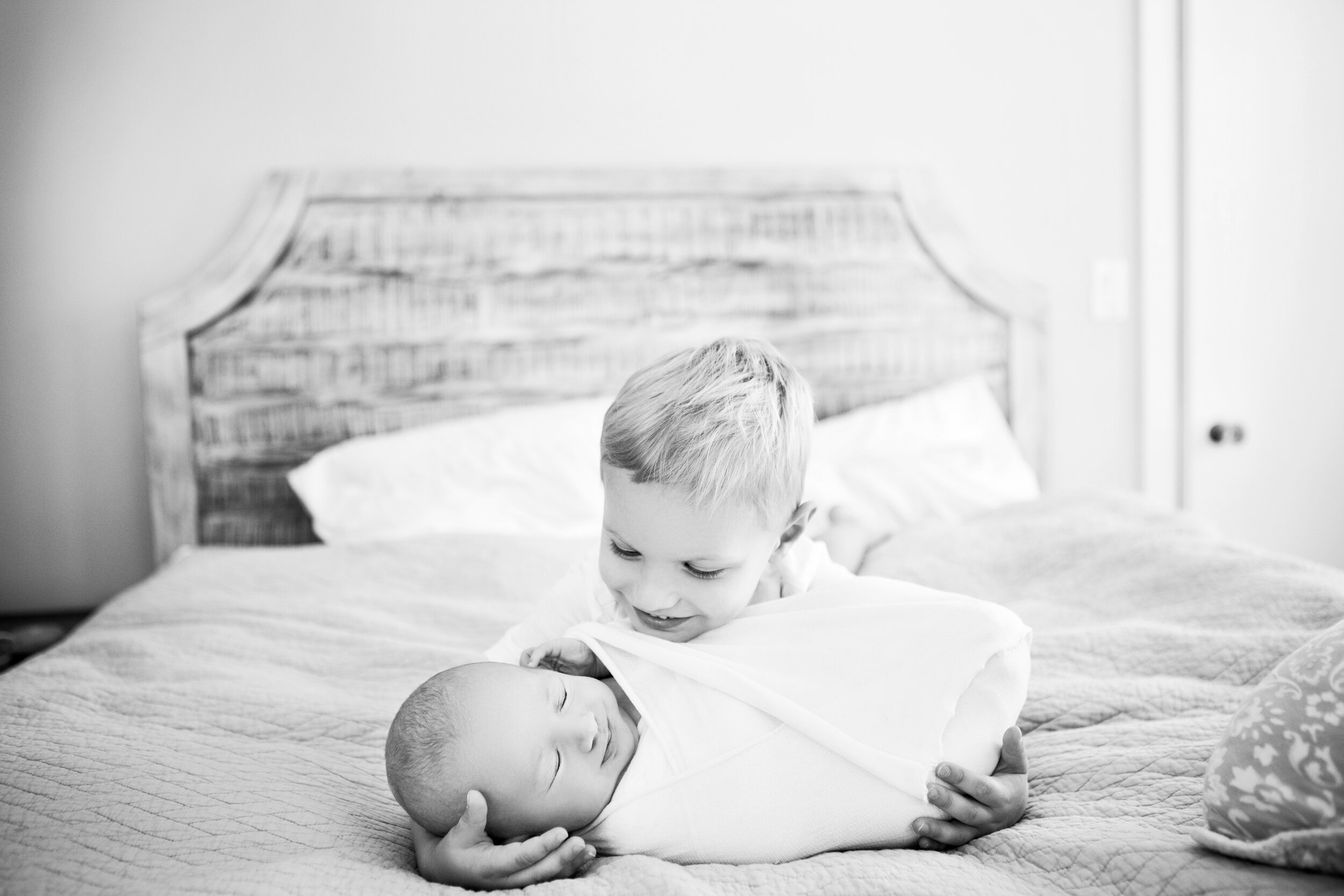 while lying on a bed, a brother smiles at his newborn baby brother