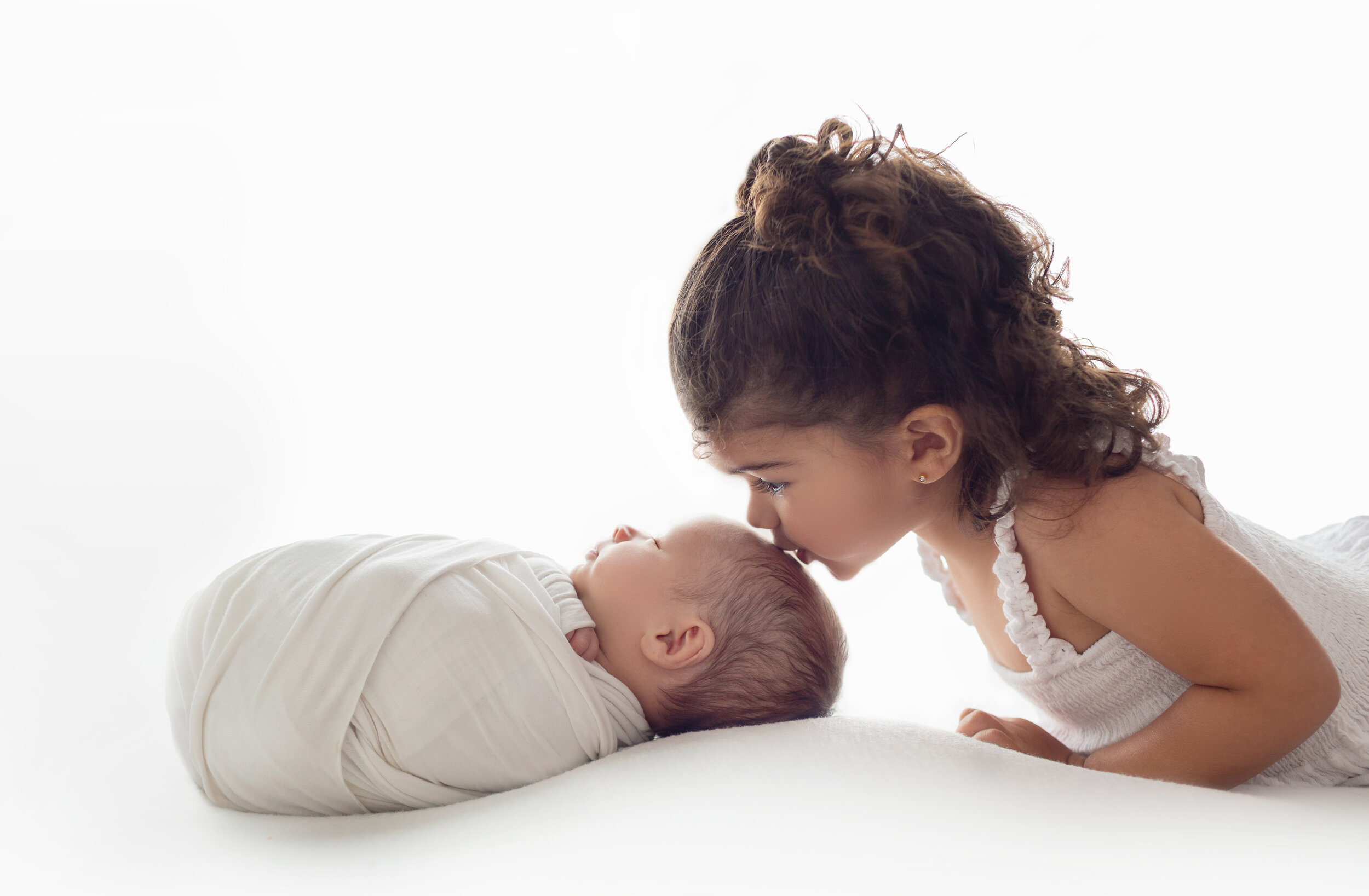 cute big sister kisses her baby brother's head in front of white light