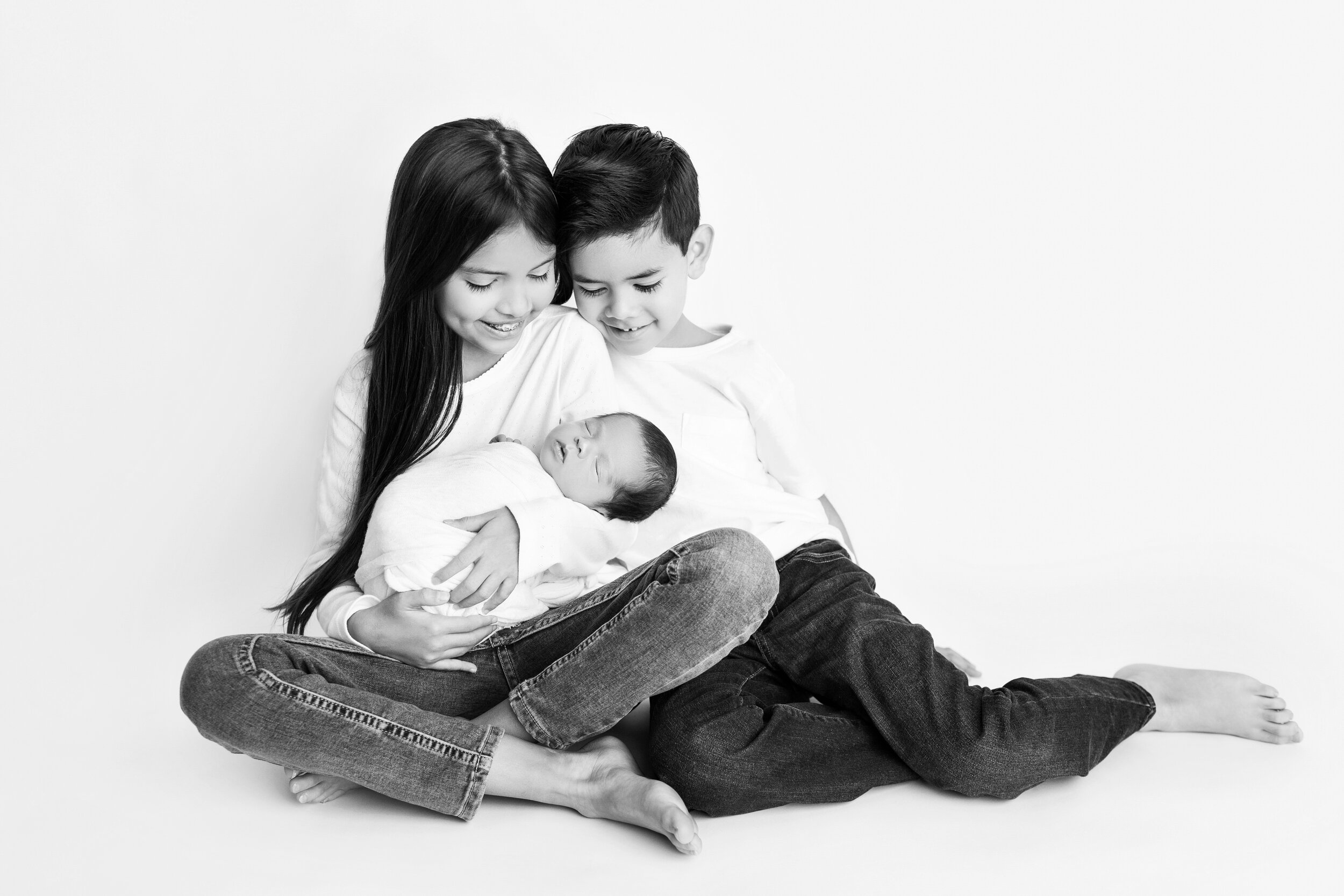 older siblings smile down at their newborn brother in black and white
