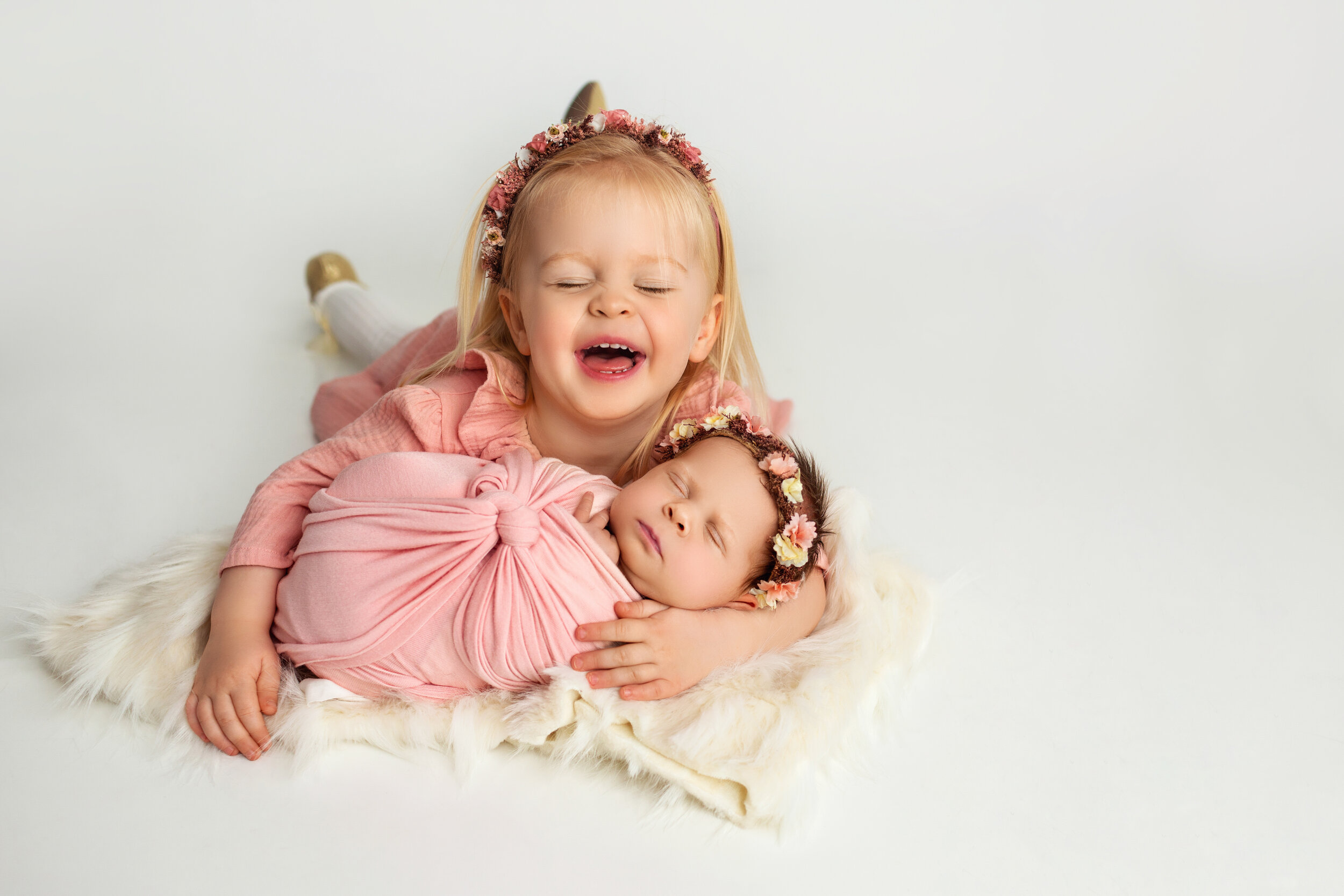 big sister laughs as she cuddles close to her new baby sister