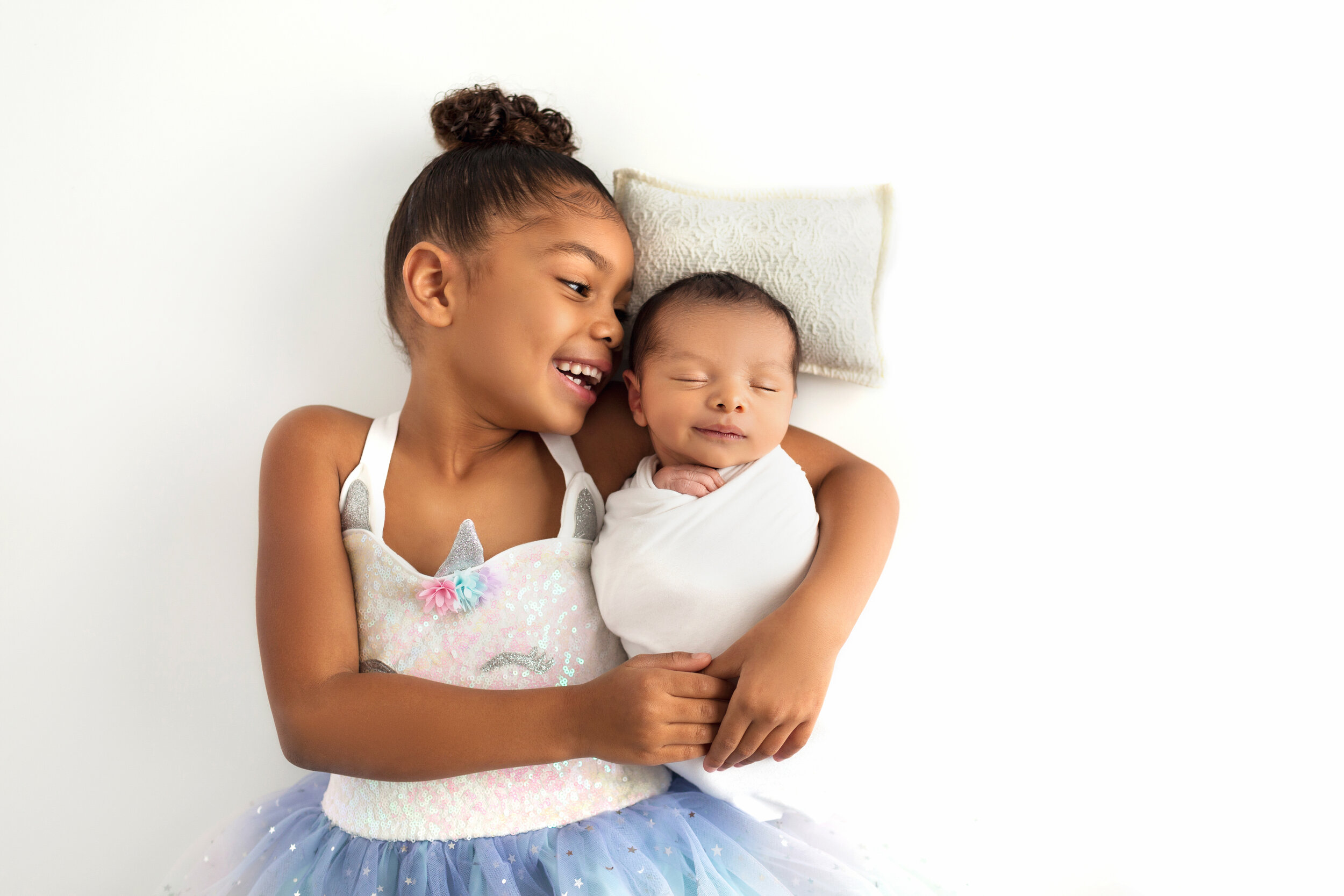 adoring big sister hugs her smiling, napping newborn brother