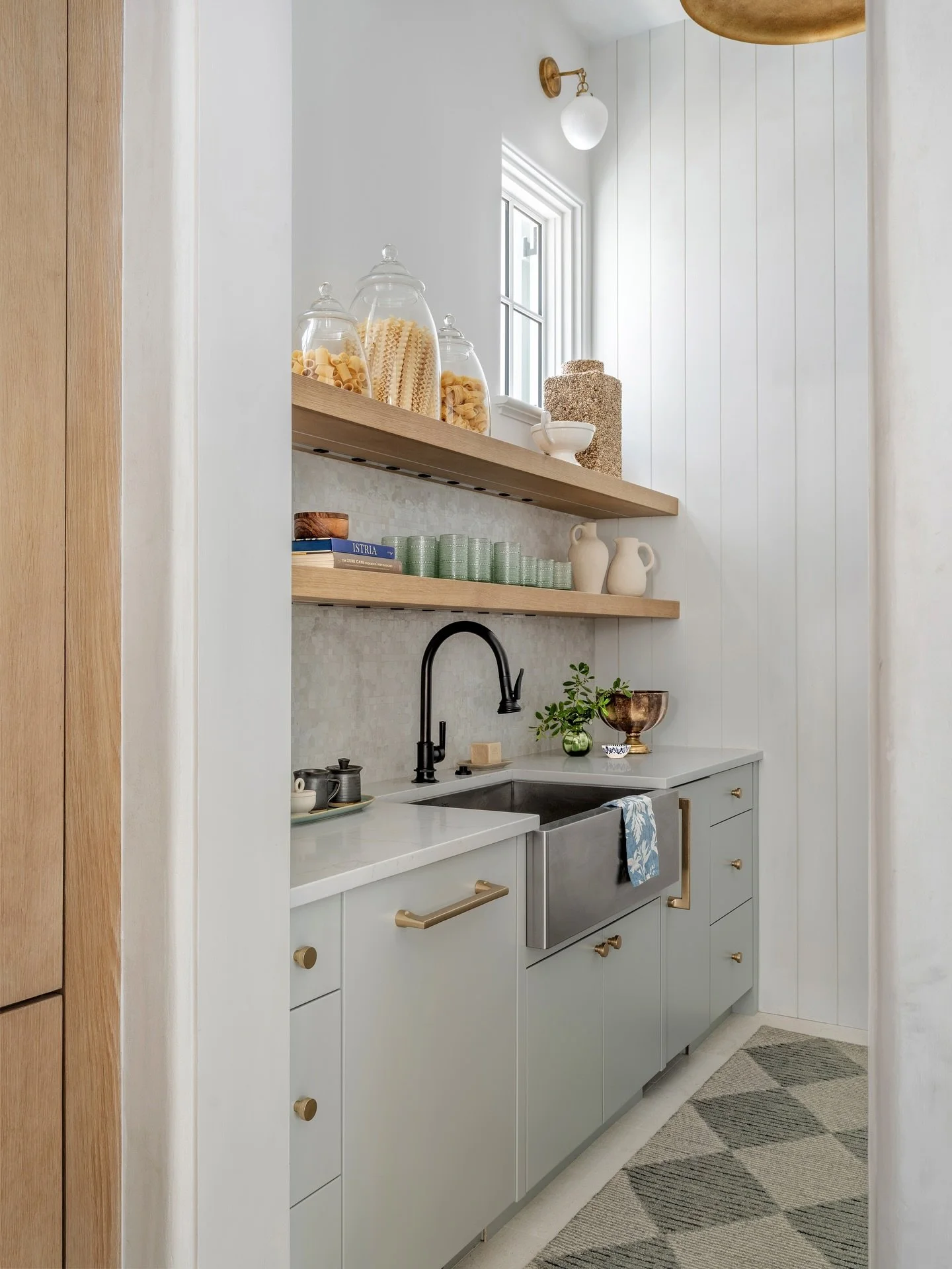 ✨ A quiet corner designed for both beauty and purpose. This scullery tucks seamlessly beside the main kitchen &mdash; with soft gray blue cabinetry, open white oak shelving, and a statement apron-front sink that balances utility with understated luxu