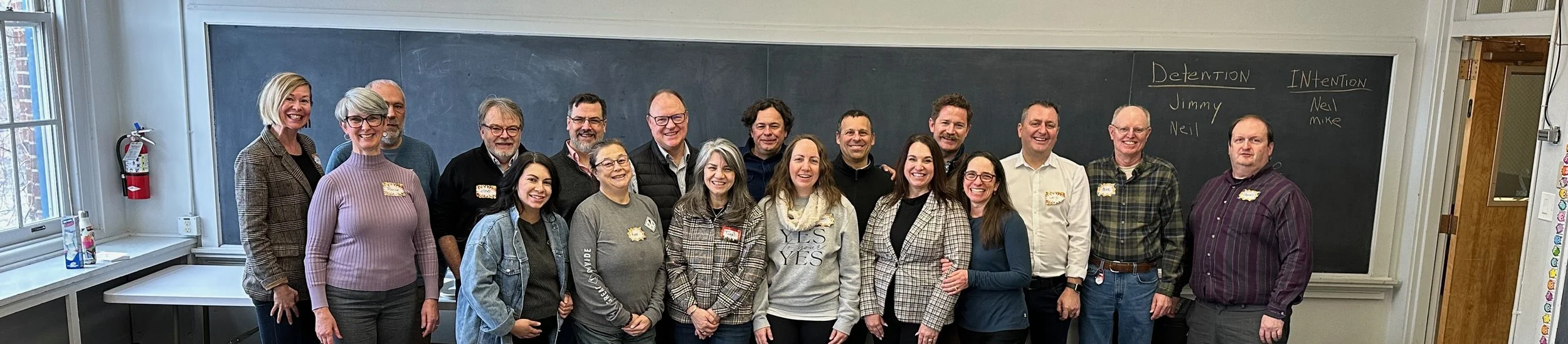 A group of people posing for a photo. They are standing in front of a chalkboard.
