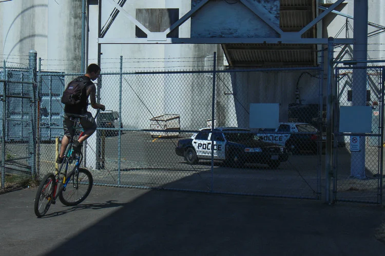 Man+rides+tall+bicycle+in+front+of+cop+cars+and+fence.jpg