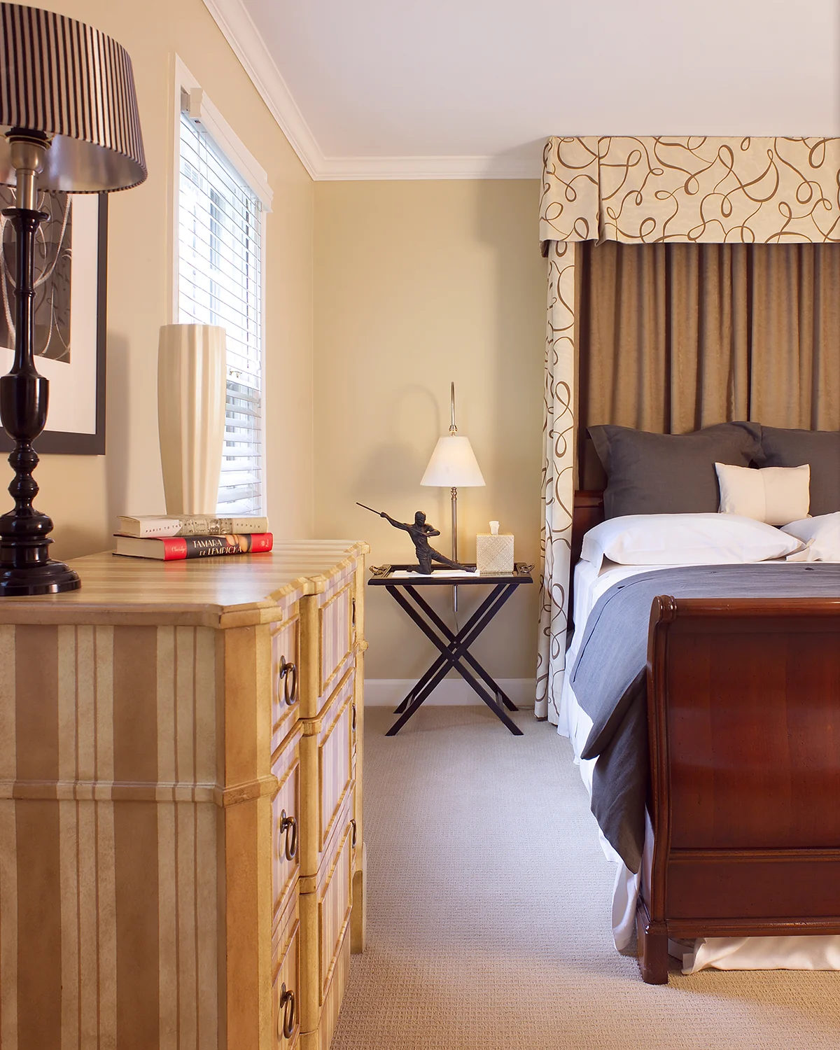 The idea was for guests to feel like royalty when staying here! For a very dramatic focal point , we took an ordinary sleigh bed and surrounded the headboard with a cornice and side drapery made of a graphic Italian fabric. On one side of the room, we added a steel desk which works as well for a vanity as it does a place to set a notebook computer. The striped, painted dresser adds another layer of texture. Details are very important when putting together the perfect guest room: we made sure to add high quality bedding and every other possible convenience to make someone feel comfortable and special. Photo by Gene Meadows.