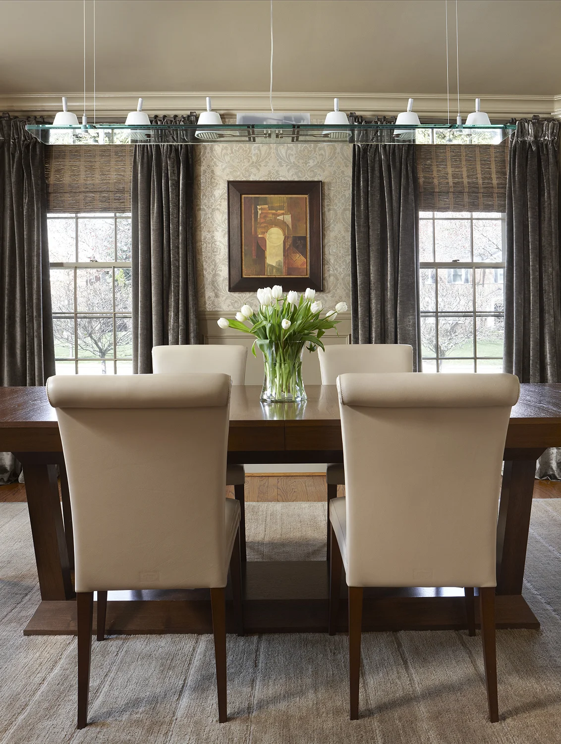 The goal in this dining room was to give a nod to the couples’ modern aesthetic while maintaining the architectural flow from outside this Colonial home. Our concept was that a young couple had inherited a Venetian palazzo. First, we raised the chair rail, and added some panel molding, then we applied a vintage looking damask wallcovering to add instant “age.” Dramatic green silk vintage linen velvet drapery and grass shades add texture. In the center of it all, contemporary Italian furniture and lighting contrast, yet compliment, the rest of the room. Photo by Beth Singer.