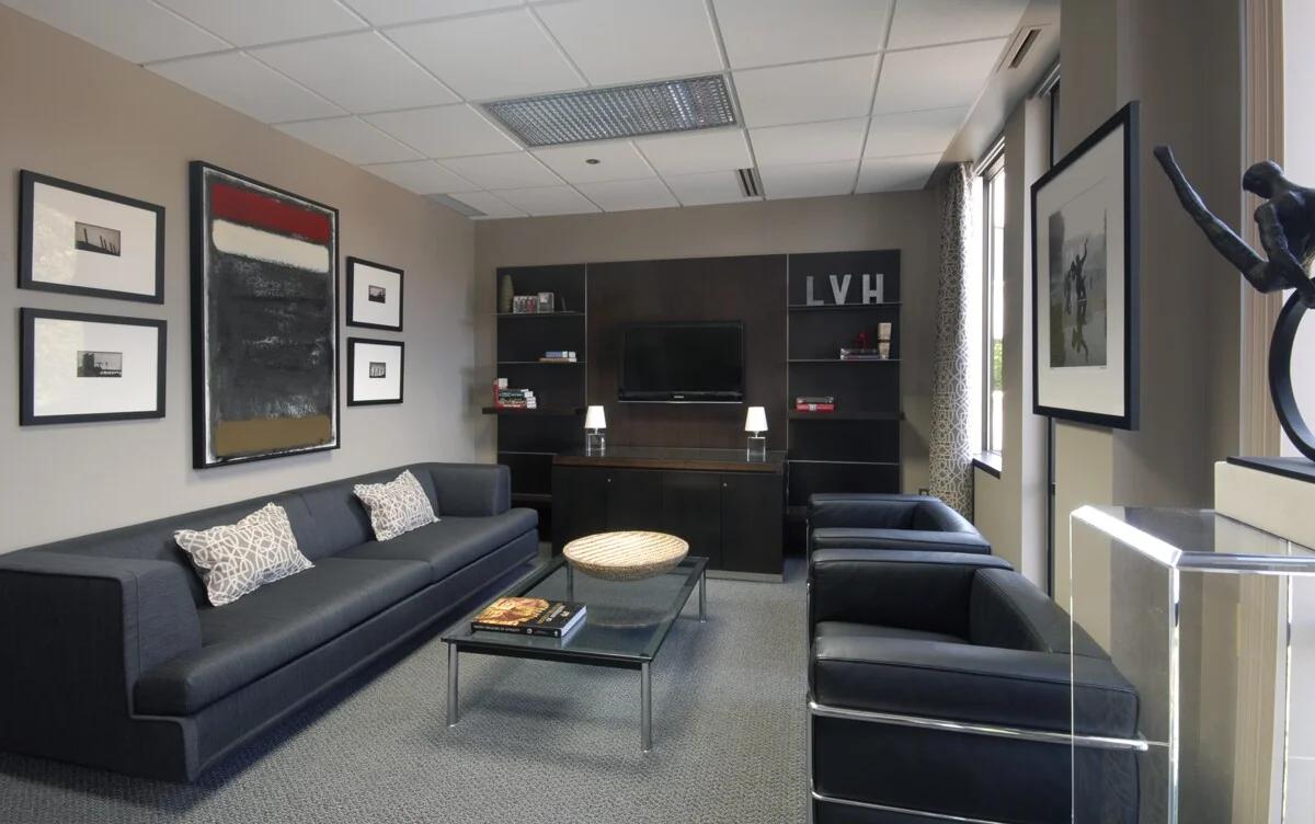 Instead of the expected traditional cherry wood furnishings, the lounge area features strong, classic modern furniture upholstered in black leather and grey wool flannel. At the far end of the space, we added a custom walnut and stainless steel wall unit composed of floating shelves, a flat-screen TV, and a bar. Black and white photography, featuring Detroit landmarks, and drapery panels complete the space. My client tells me he’s more productive than ever.