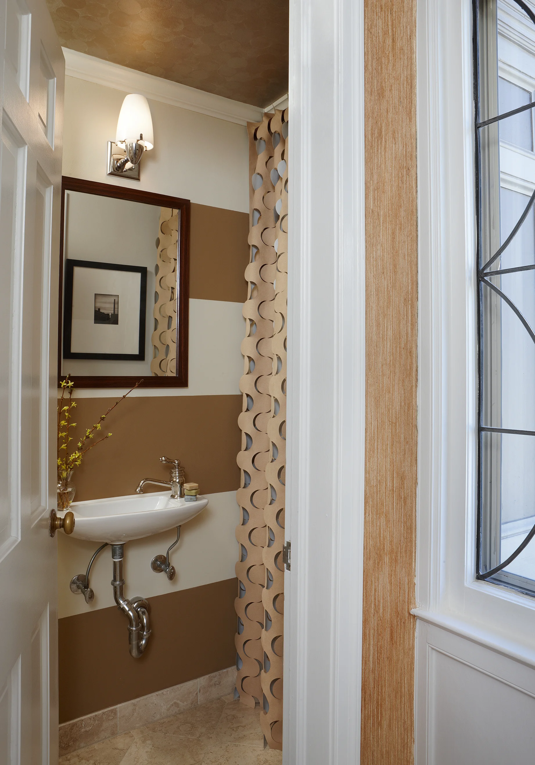 Petite spaces are a great way to use luxurious materials and go for over-the-top style–a powder room should always be a surprise for guests. We painted the walls in bold stripes to visually “widen” the space, and papered the ceiling with an elegant silver leaf. The laser-cut drapery fabric becomes sculpture and adds dimension to the room. Photo by Beth Singer.