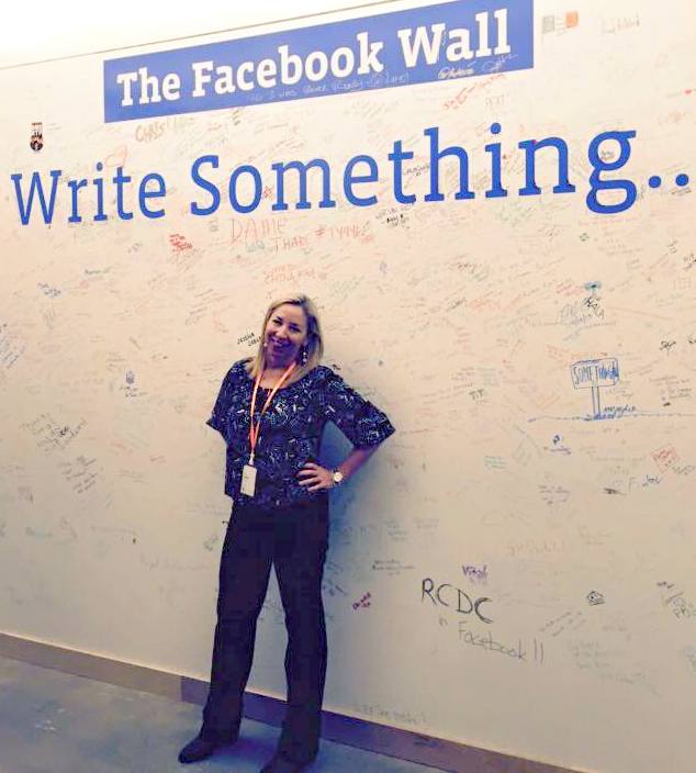Sande Snead poses in front of the real Facebook wall at their offices.