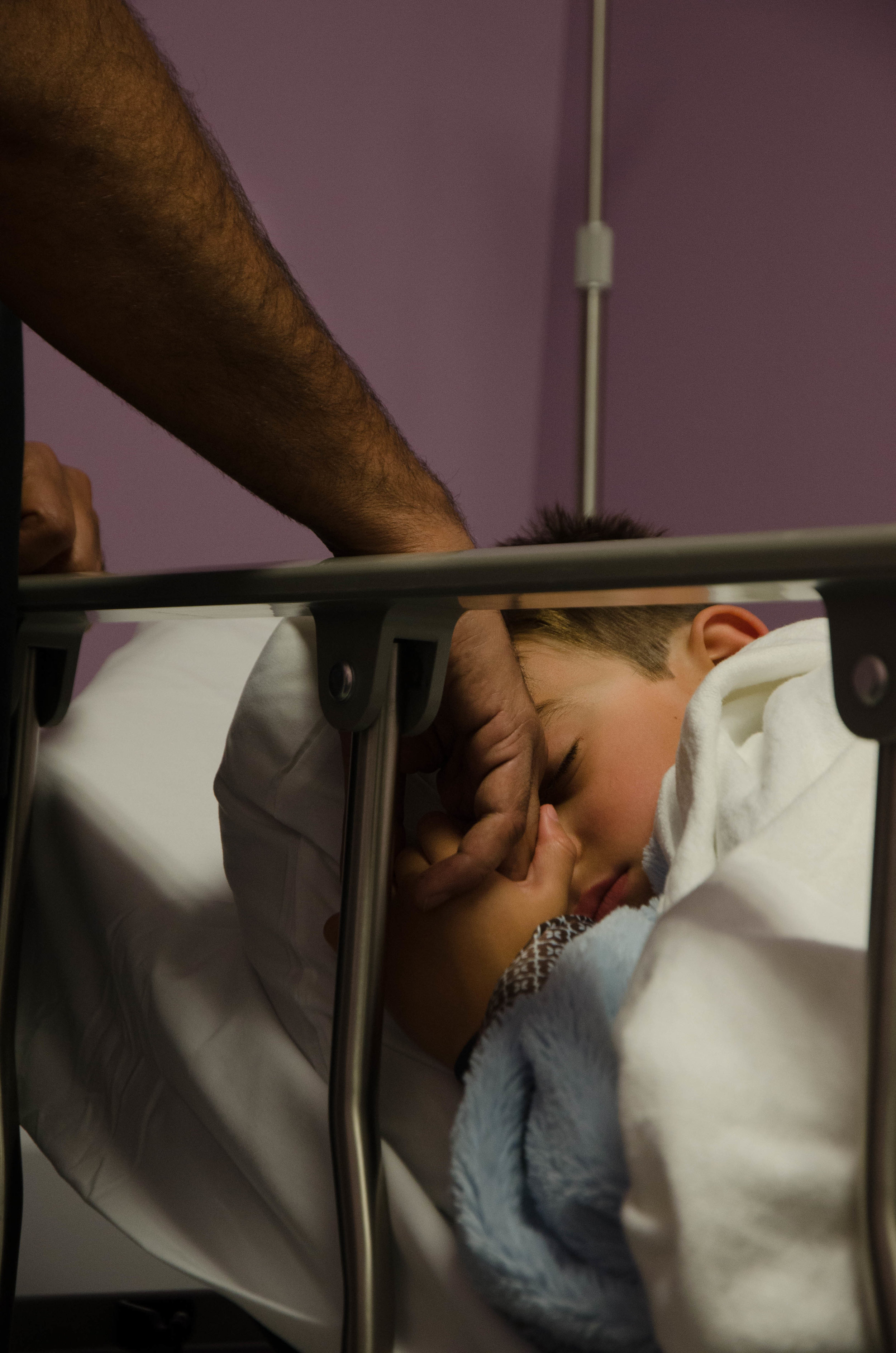  Dax Thakker falls asleep in a hospital bed as he holds his father Anooj Thakker’s hand before surgery. 