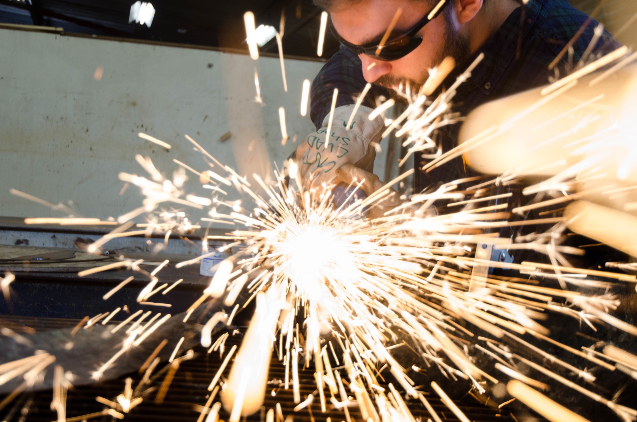 Brandon McGahey welds part of the metal arm for his handmade chair while wearing protective glasses in the art building’s shop.