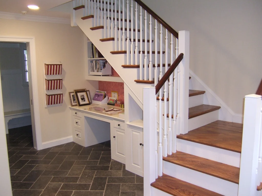 Home interior featuring a staircase with wooden steps and white spindles, a built-in desk with framed photos and books, and a hallway with brick-patterned tile flooring.