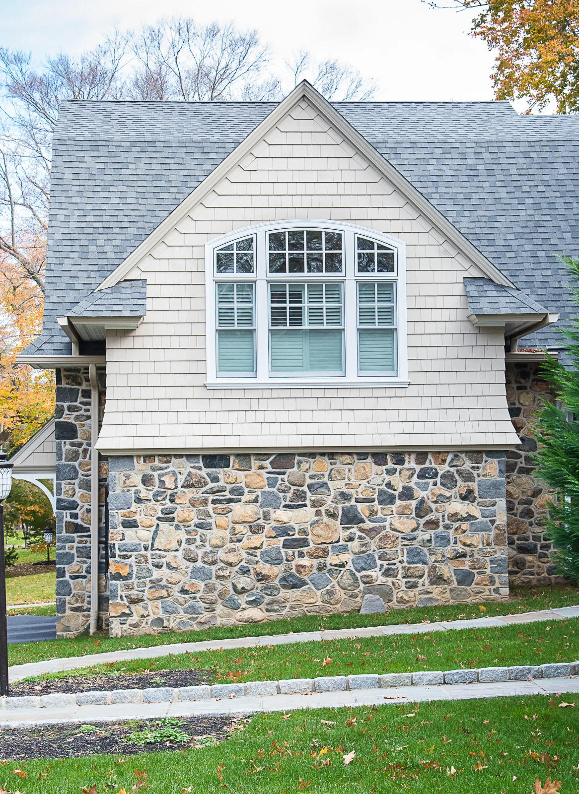 Front view of a house with stone and siding exterior, large arched window with shutters, and a well-maintained lawn.